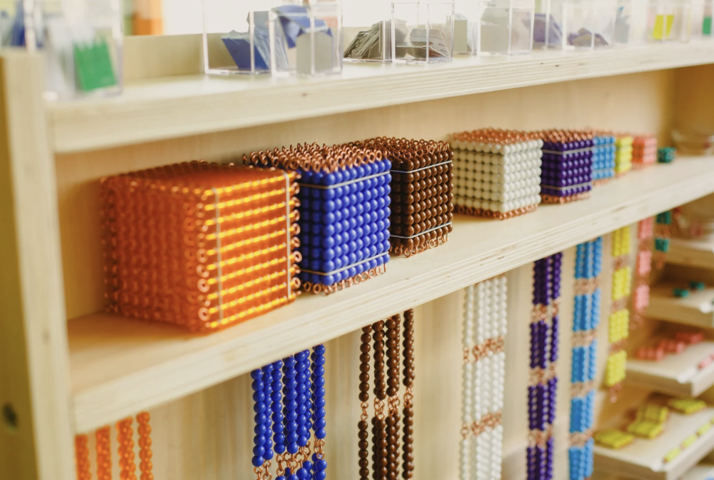 Colourful Montessori golden bead and place value materials displayed on wooden classroom shelves.