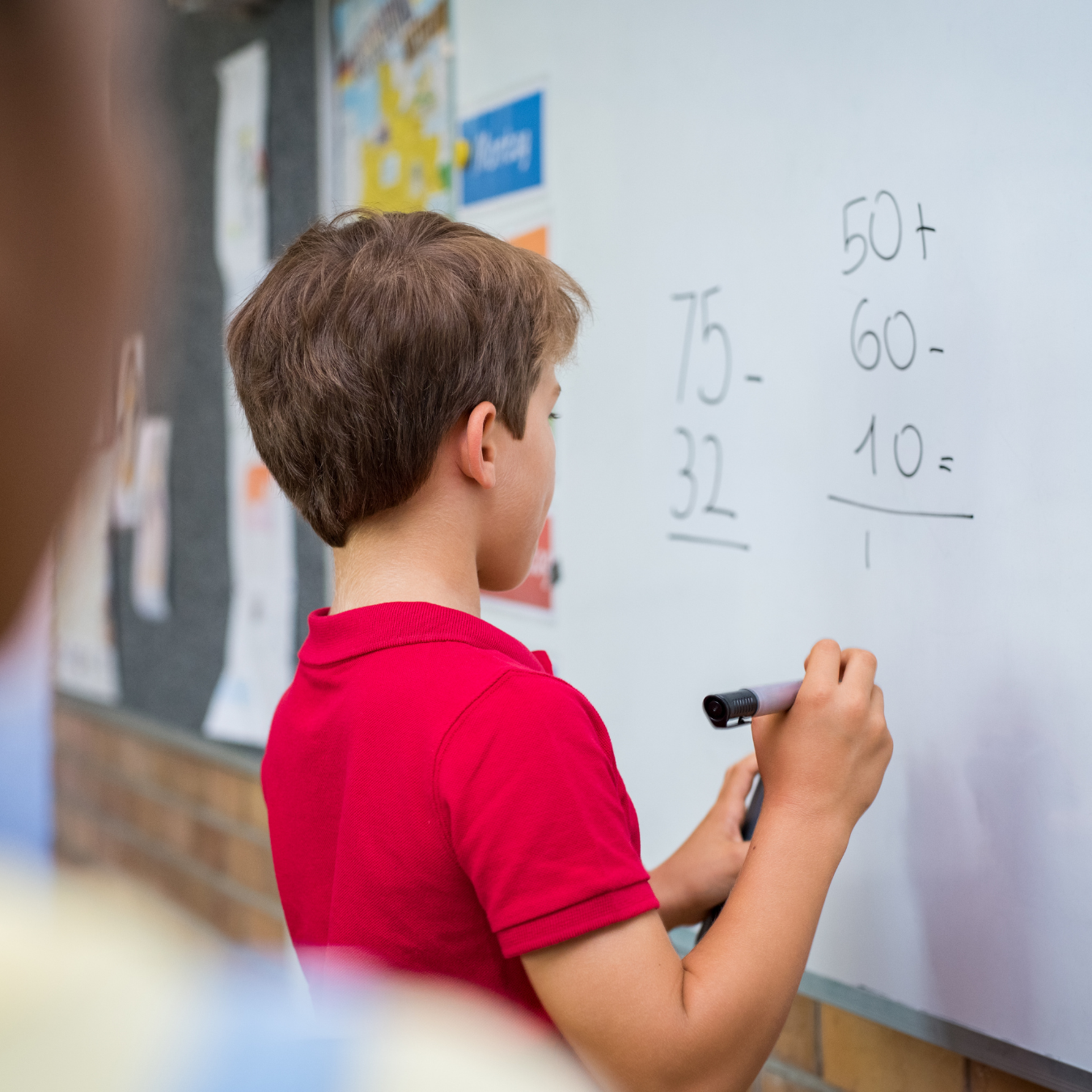 Student writing math problems on a whiteboard during a classroom lesson.