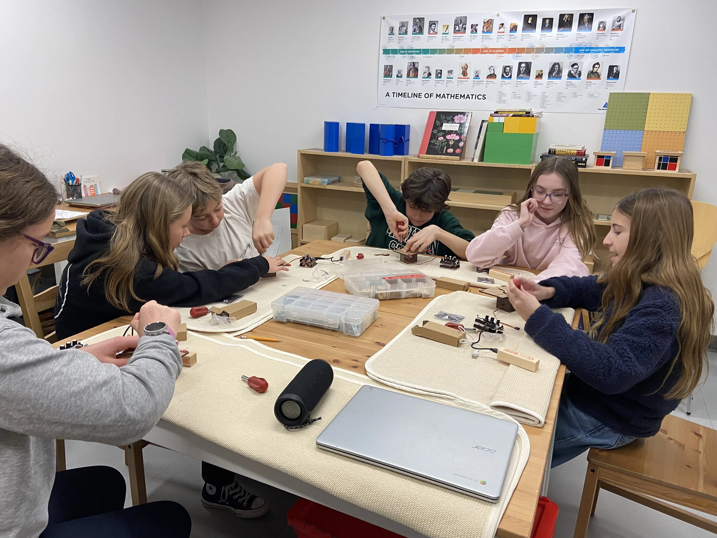 Adolescent students working together around a classroom table during a hands-on Montessori learning activity.