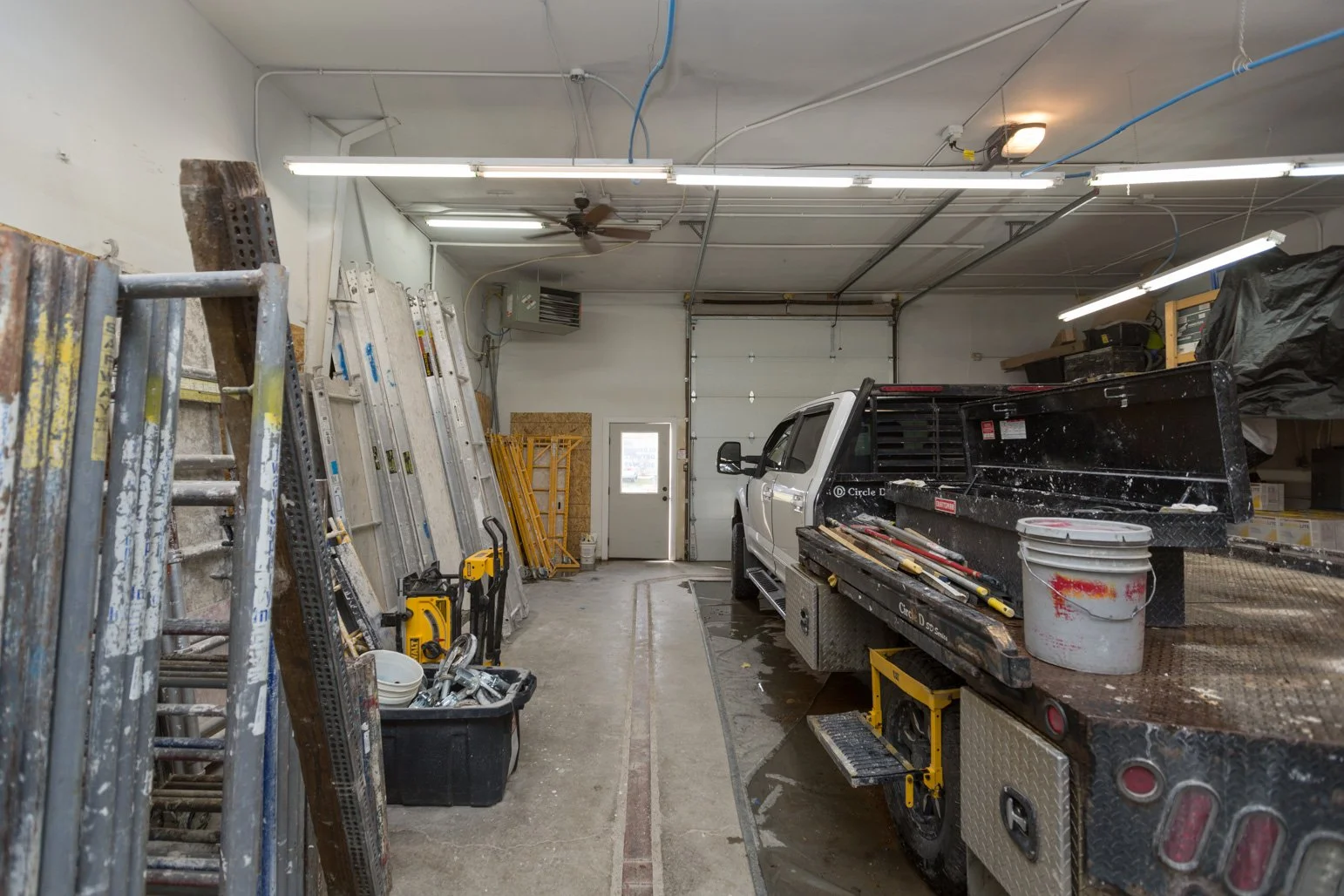 Interior of Olbricht Drywall workshop or garage with ladders, tools, and a work truck parked inside.