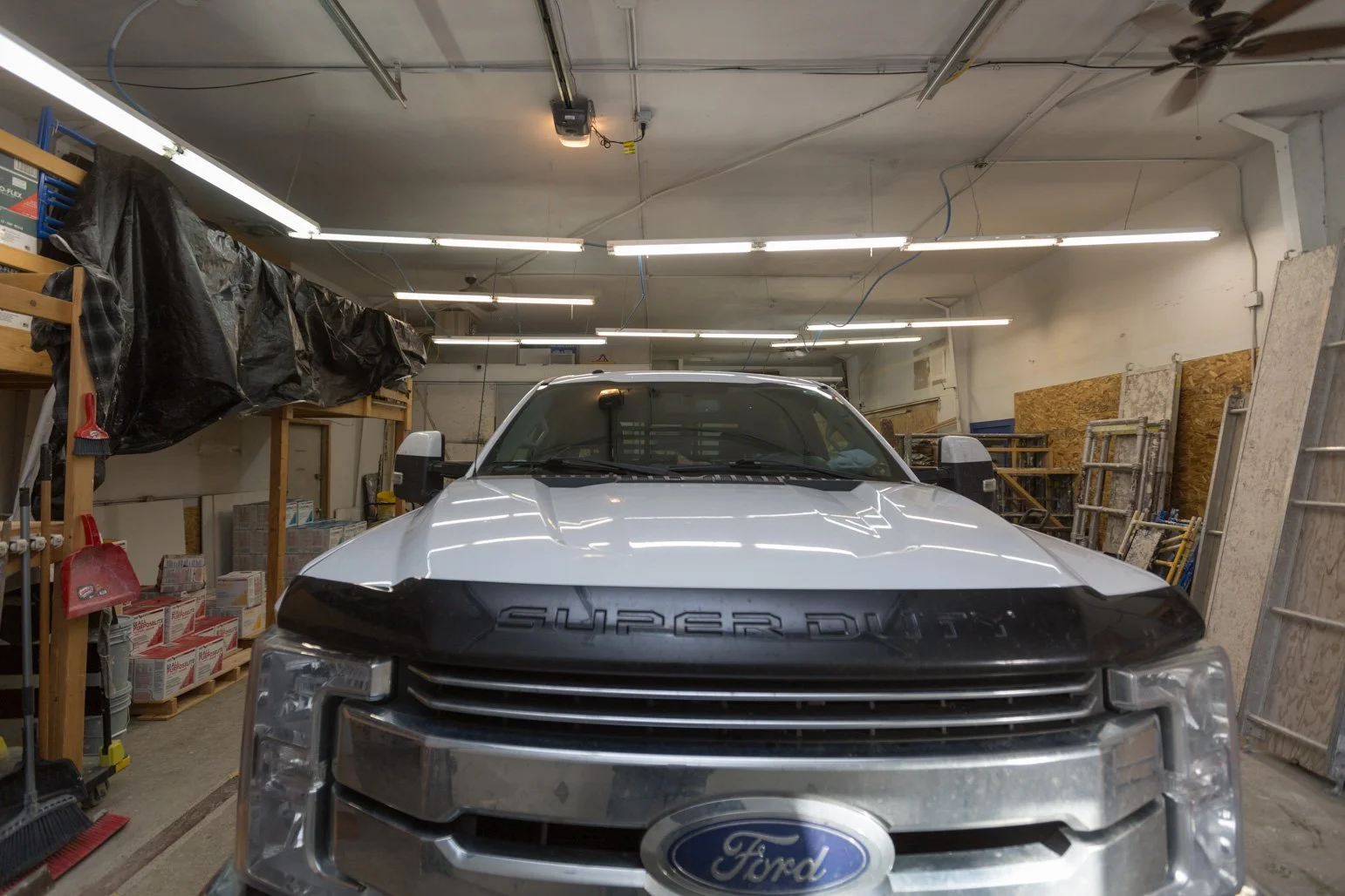 Front view of a Olbricht Drywall truck inside a garage or workshop with tools, shelving, and materials.