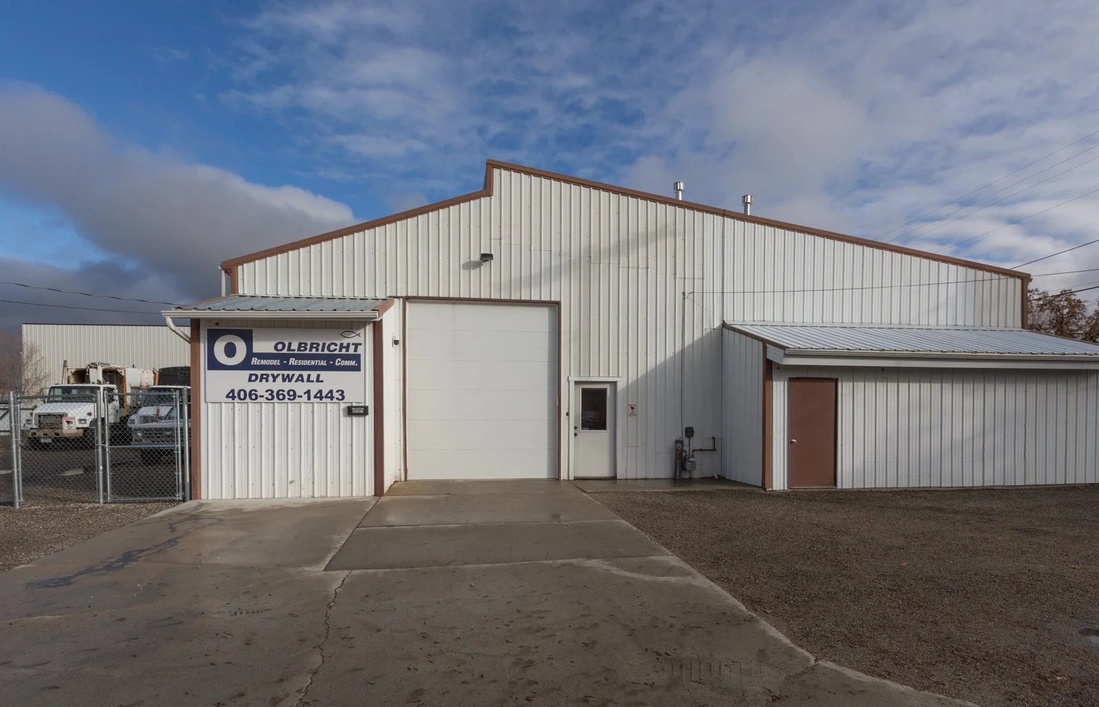 Exterior of 'OLBRICHT Drywall', white building with multiple doors and ample parking space.