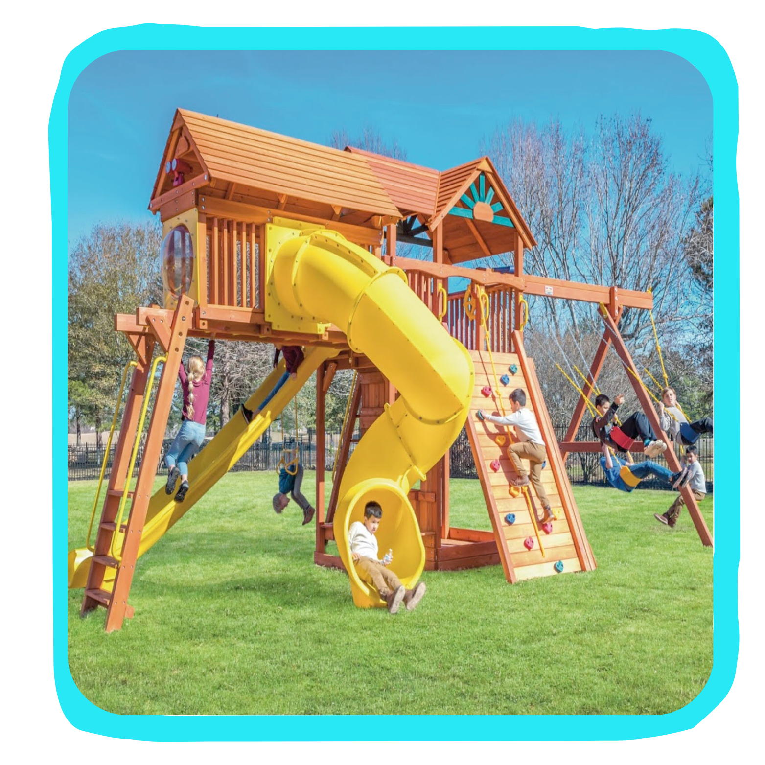 Children playing on a large wooden playset with a yellow slide, climbing wall, swings, and a small house structure, outdoors on a grassy field with trees and a blue sky.