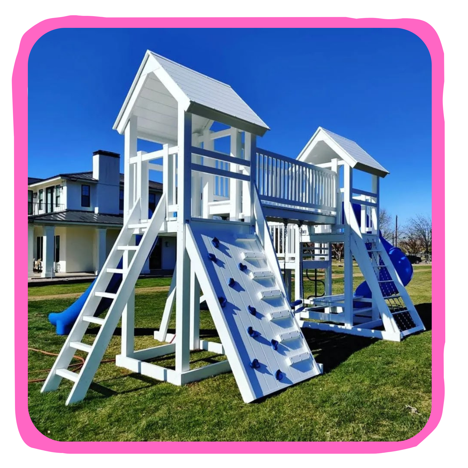 White wooden outdoor play structure with multiple slides, climbing walls, and a bridge, set on grass in a residential area.