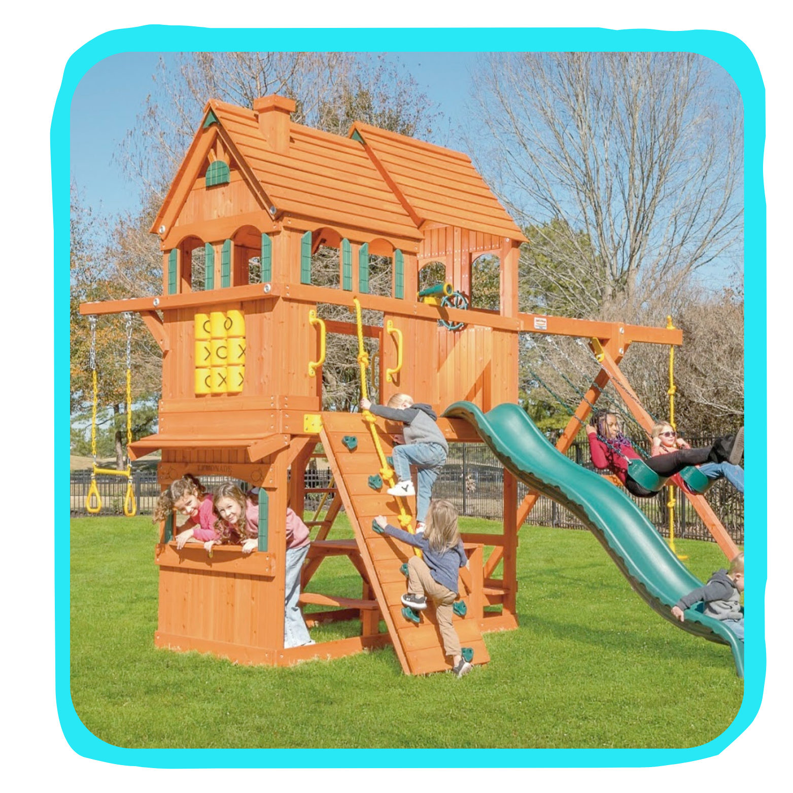 Children playing on a wooden playground structure with slides and swings on a grassy field, trees in the background.