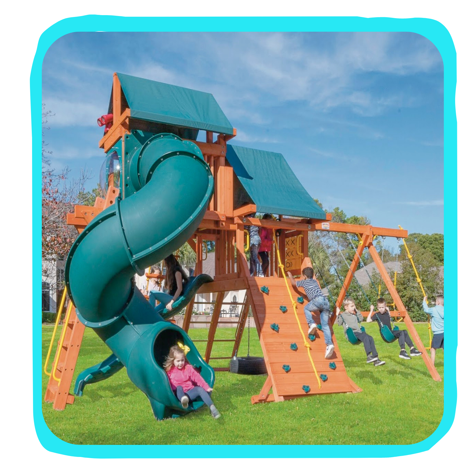 Children playing on a wooden playground set with a green slide, climbing wall, swings, and a shaded playhouse on a grassy field under a blue sky.
