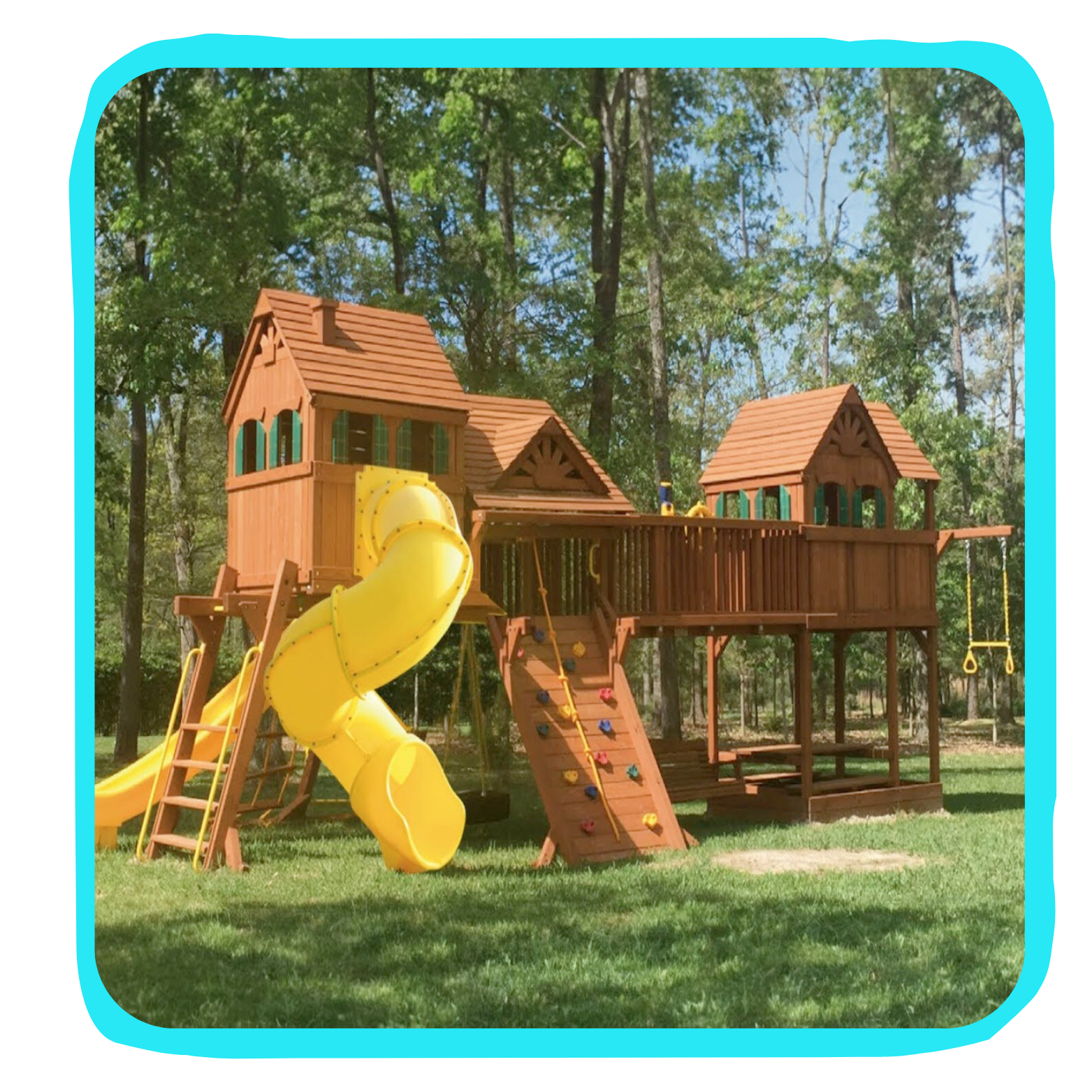 Wooden playground structure with yellow slide, climbing wall, swings, and treehouse-style towers in a grassy yard surrounded by trees.