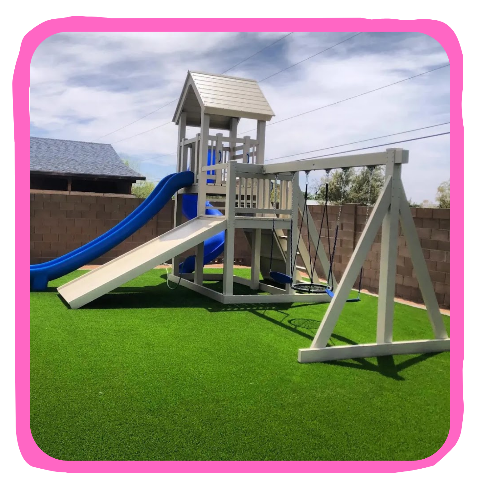 A backyard playground set with a slide, swings, and a playhouse, situated on green artificial turf with a brick wall and blue sky in the background.