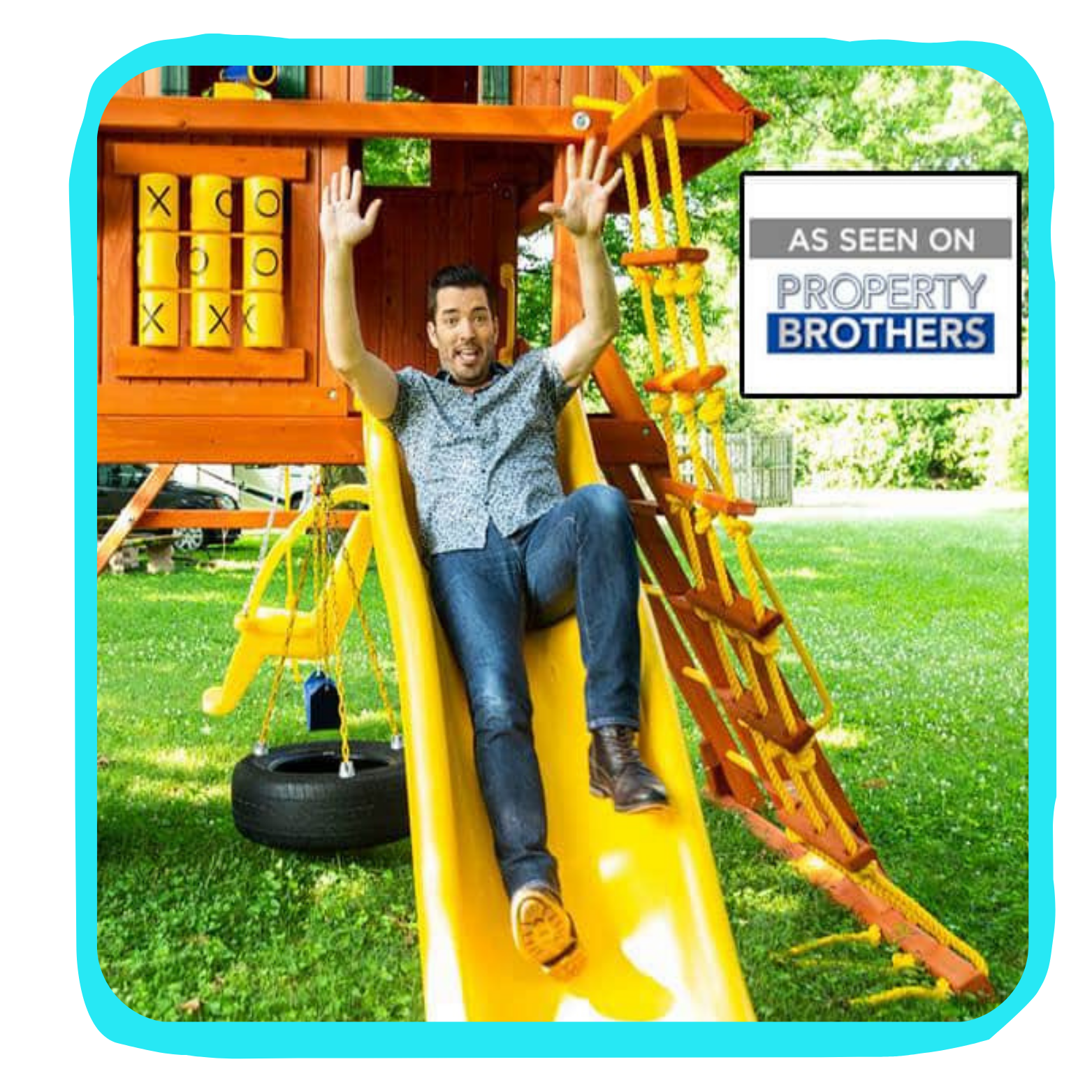 A man sitting on a yellow slide at a wooden playground, with a tire swing and climbing ropes, in a grassy yard with trees. There is a sign that says "As seen on Property Brothers."