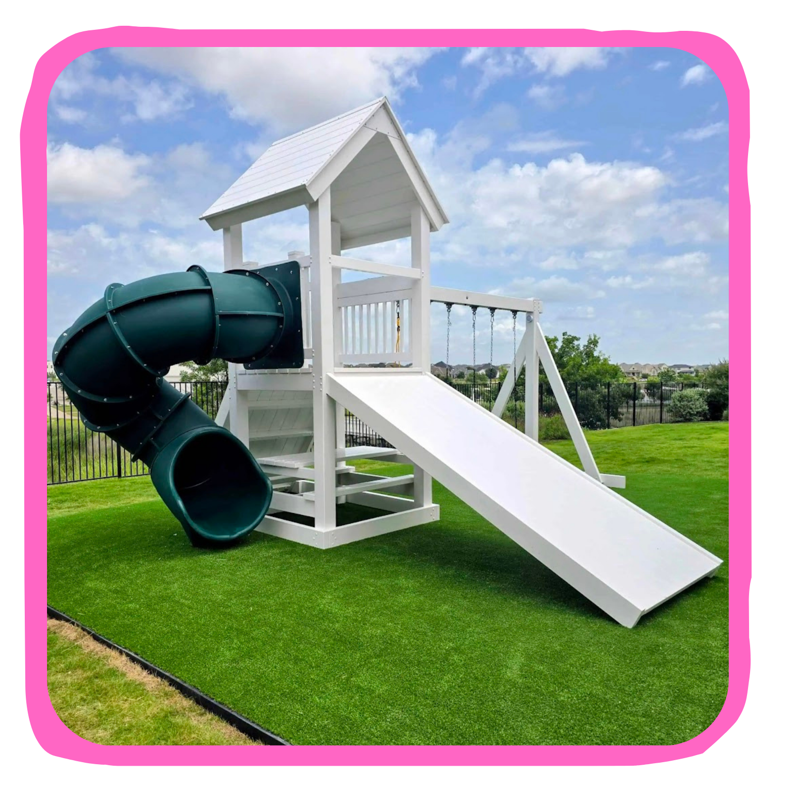 Outdoor white wooden playset with slide and tube tunnel on green grass under partly cloudy sky.
