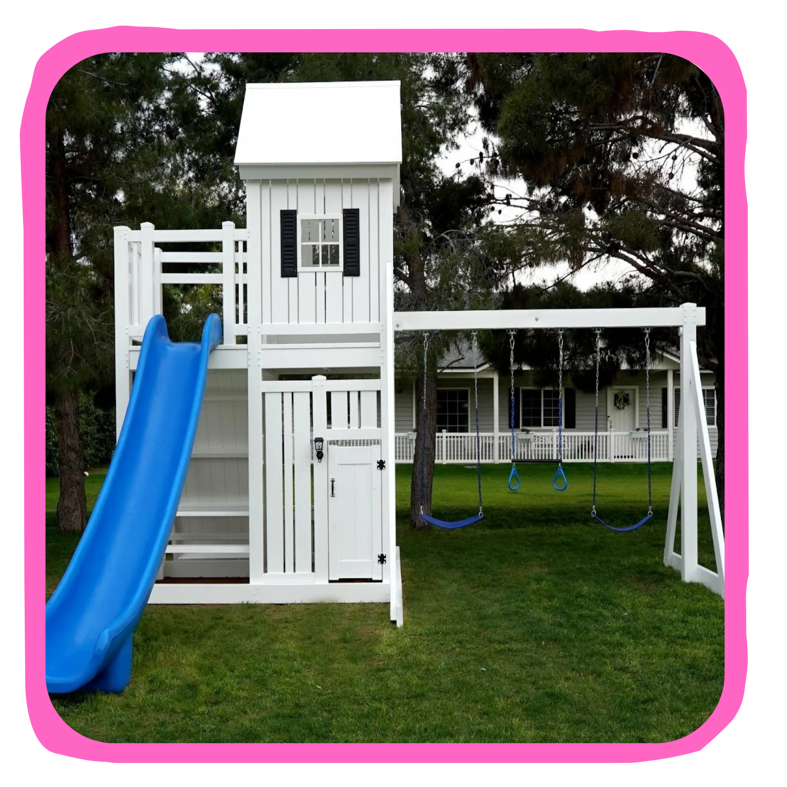 White outdoor playset with a slide, swings, and a small house structure, situated on a grassy yard with trees and a house in the background.