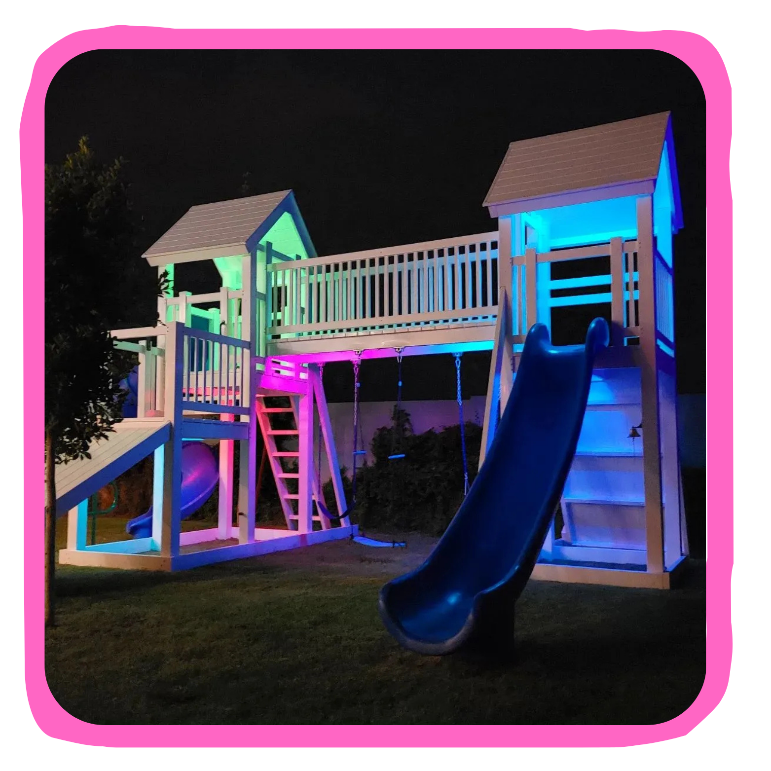 Nighttime view of a wooden playground structure with slides, swings, and ladders illuminated by colorful LED lights.