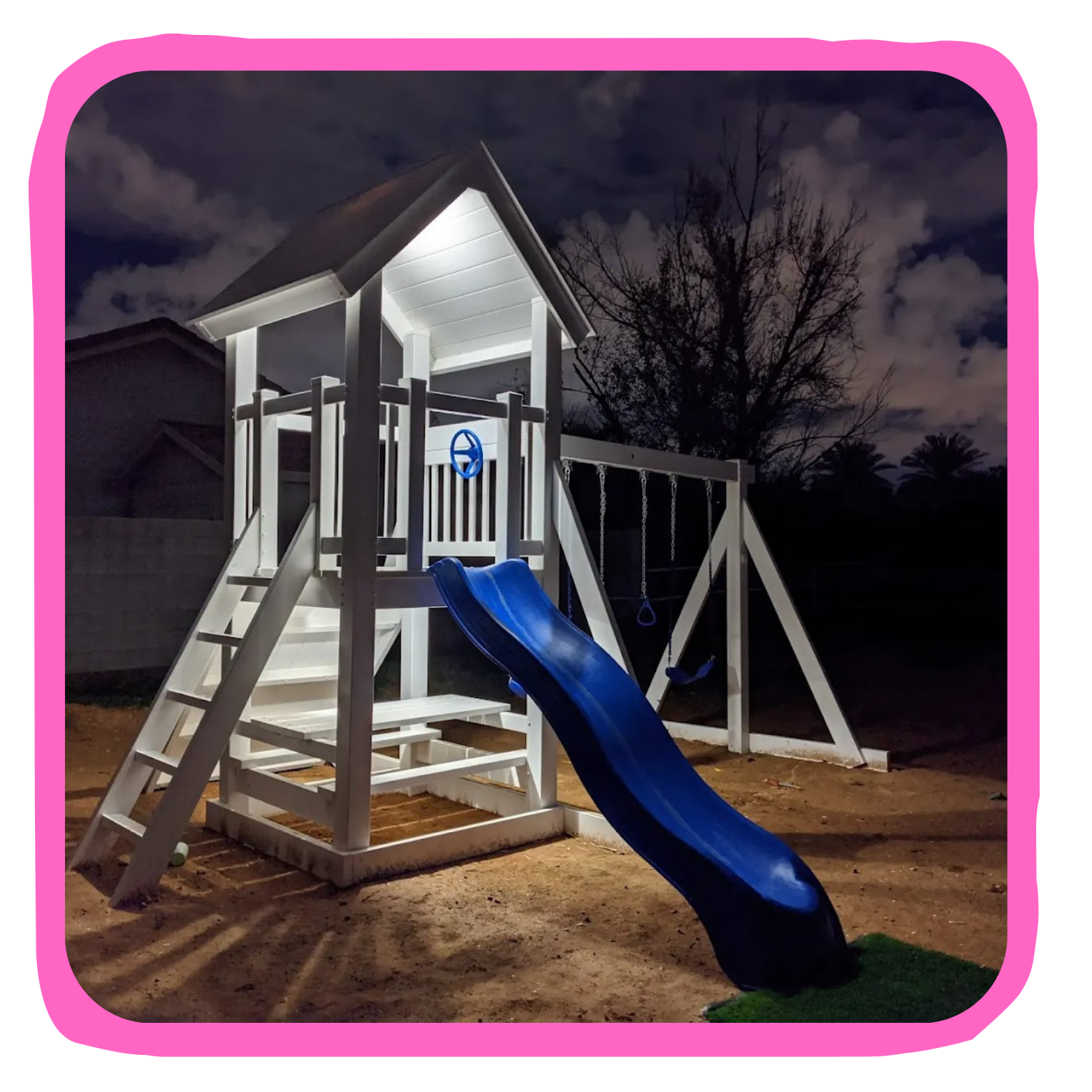 Children's outdoor playset at night with slide, swings, and climbing ladder, illuminated with bright lights against a dark sky with clouds and trees in the background.