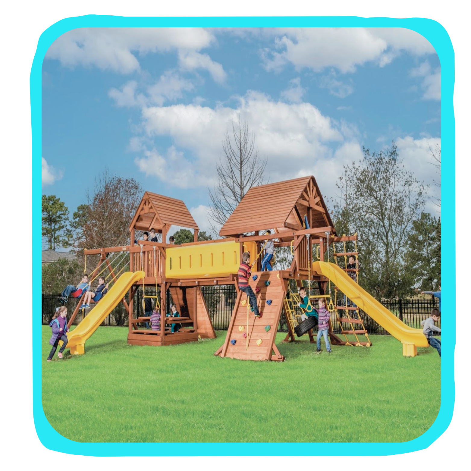 Children playing on a large wooden playground structure with slides, climbing walls, and swings, set in a grassy park under a blue sky with scattered clouds.
