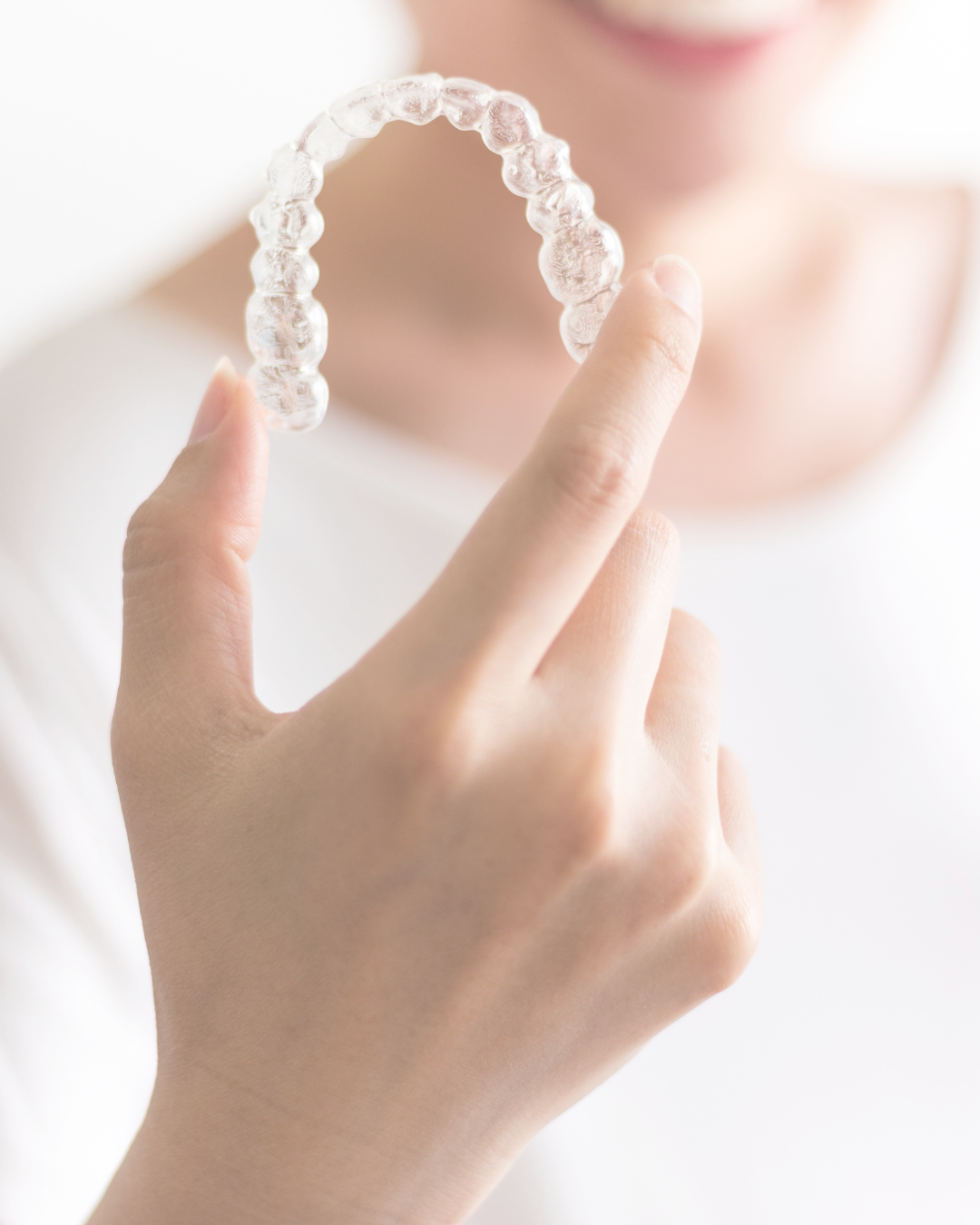 Person holding a clear dental aligner near their face, showing it up close.