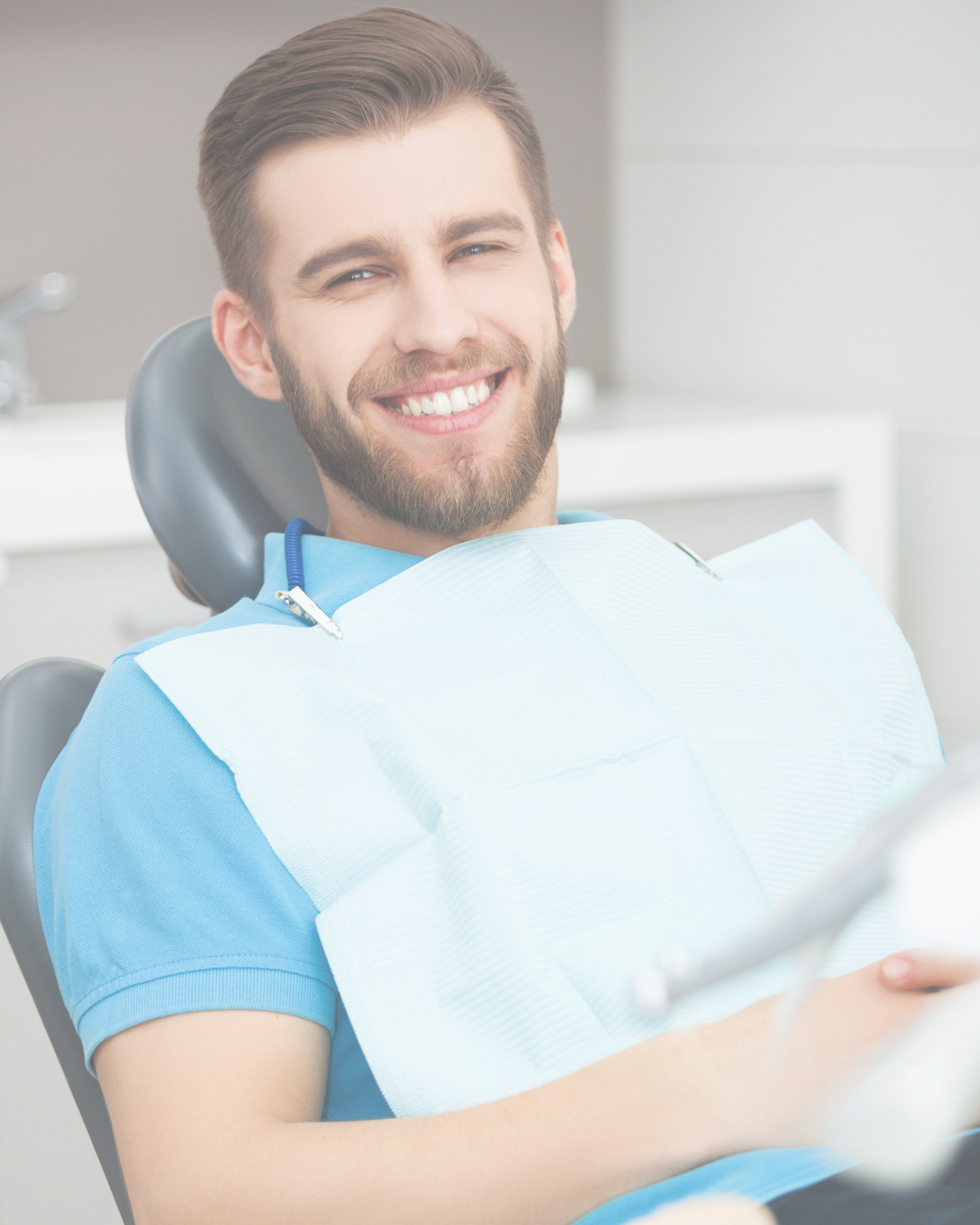 A smiling man in a blue shirt sitting in a dental chair with a dental bib, in a dental office.