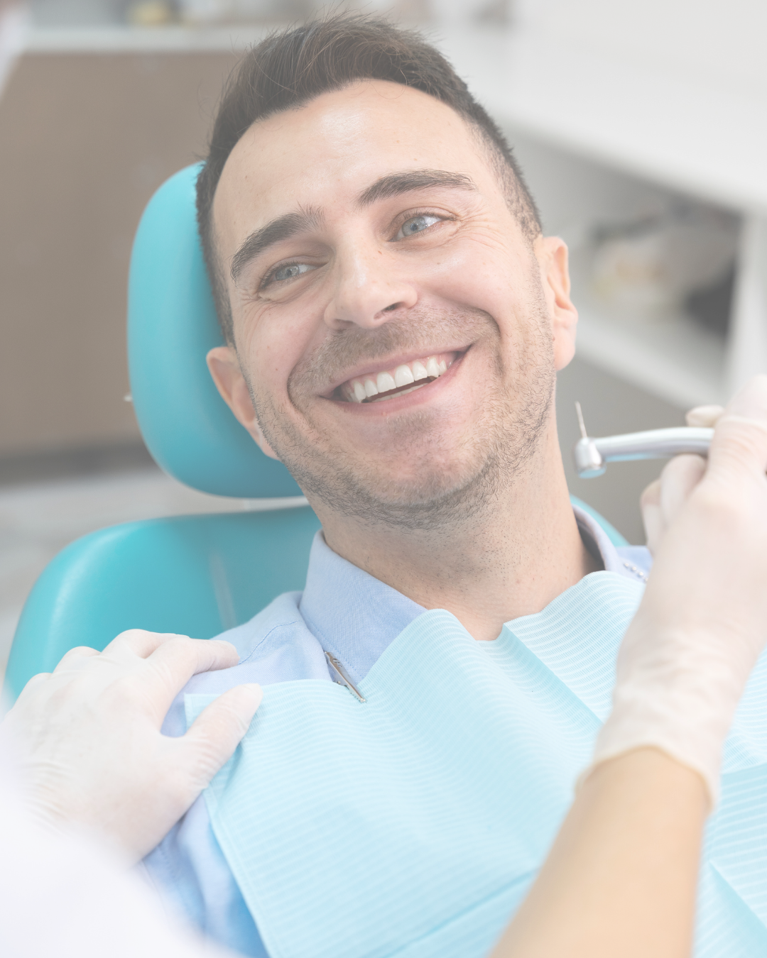 A smiling man at the dentist's office, sitting in a dental chair, wearing a blue dental bib, with a dental tool in hand, and a dental professional with gloved hands gently touching his shoulder.