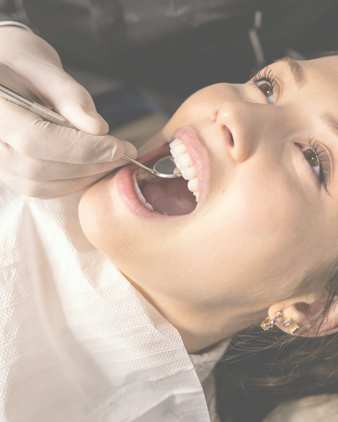A woman receiving a dental exam with a dental mirror in her mouth at the dentist's office.