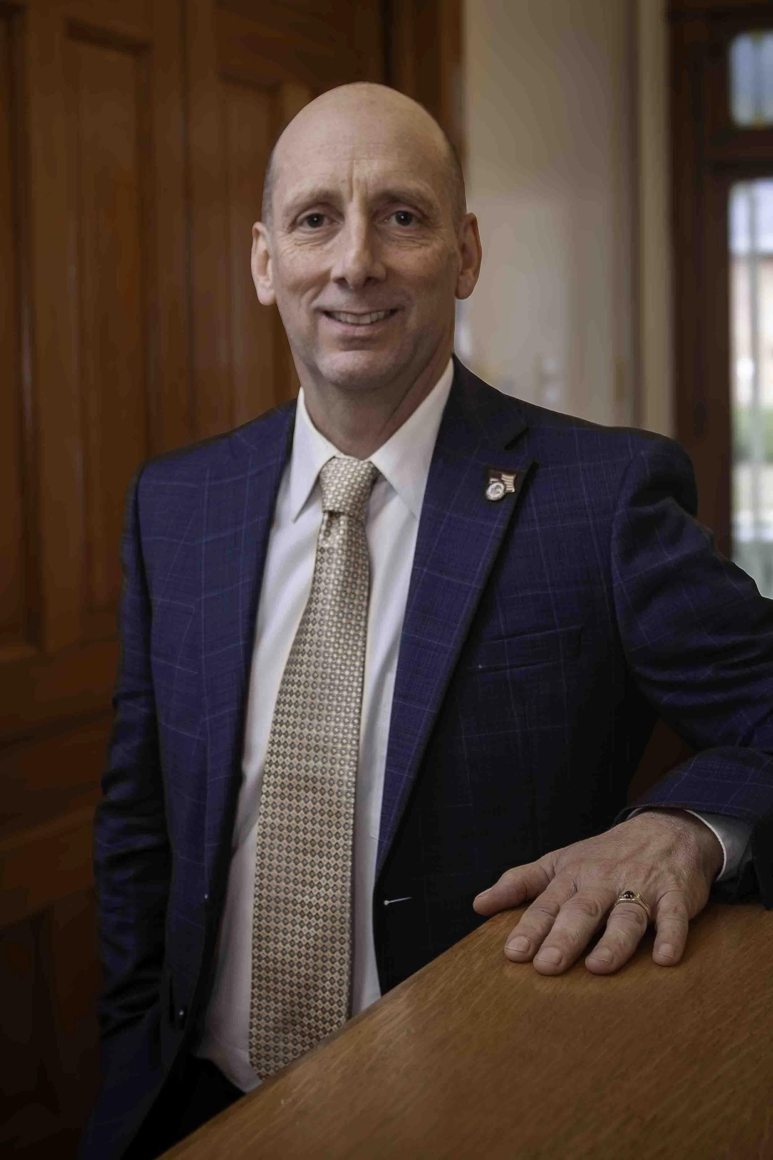 Mike Lockridge, attorney, man standing in a law building in a dark blue checkered suit, white shirt, and beige patterned tie, and smiling
