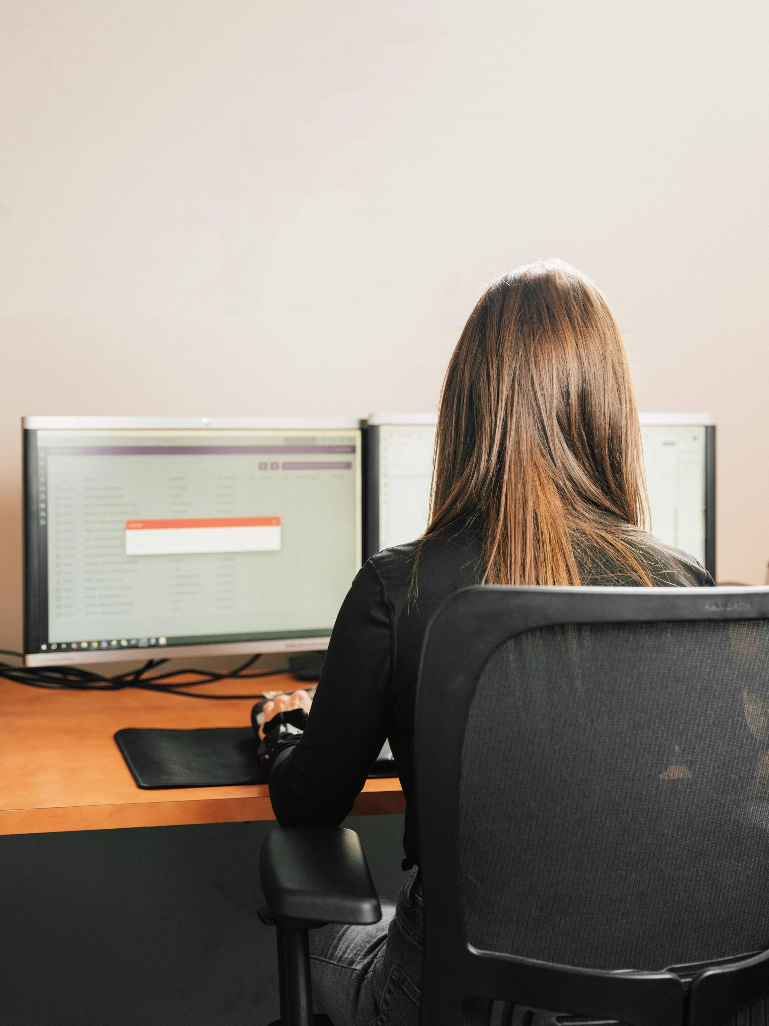 Une femme avec des cheveux bruns travaillant sur un ordinateur à double écran dans un bureau.