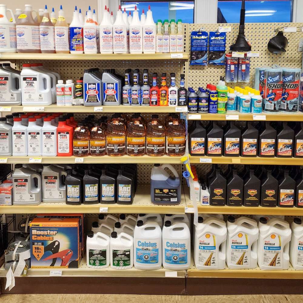 Rayonnage avec divers produits pour l'entretien et la réparation automobile, y compris des liquides, des huiles, des produits de nettoyage, et des câbles pour démarreur.