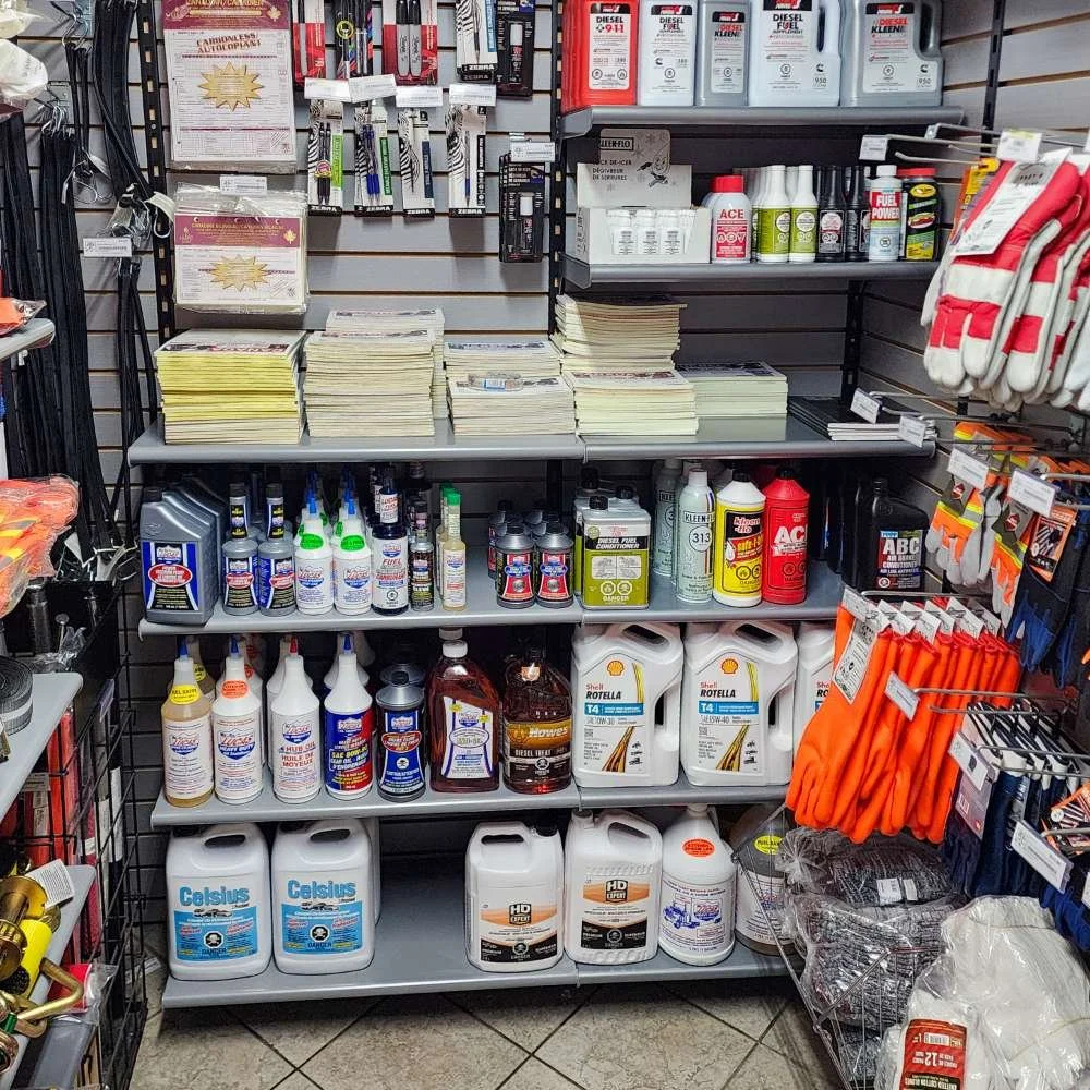 Rayonnage dans un magasin avec divers produits, y compris des huiles pour moteur, des produits de nettoyage, des gants de travail, et des accessoires automobiles.