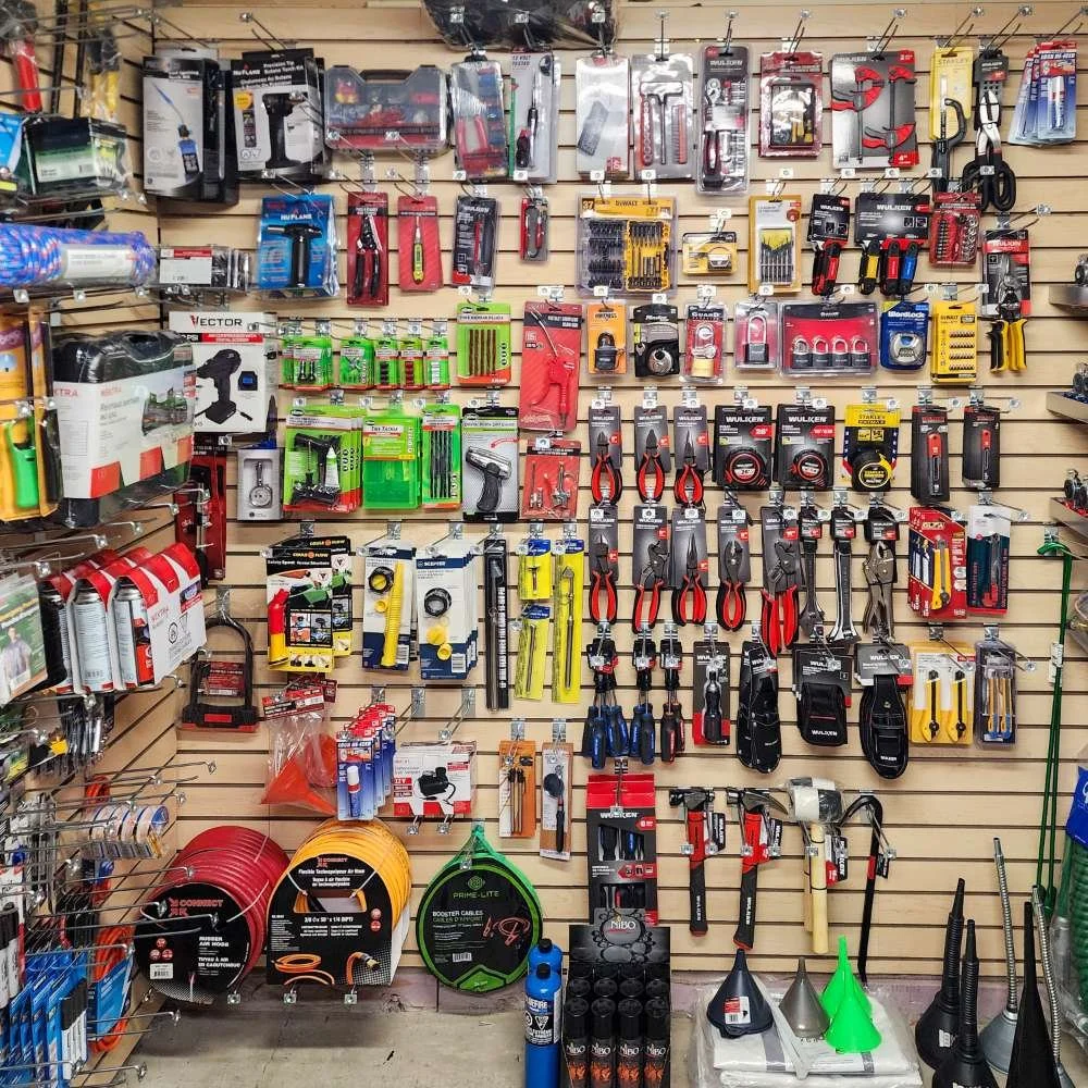 Étagère avec divers outils manuels et électriques pour la maison et le bricolage, y compris tournevis, pinces, câbles de démarrage, pistolets à calfeutrer, et autres accessoires