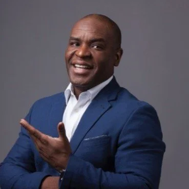 A man in a blue blazer and white shirt smiling and pointing to his right.