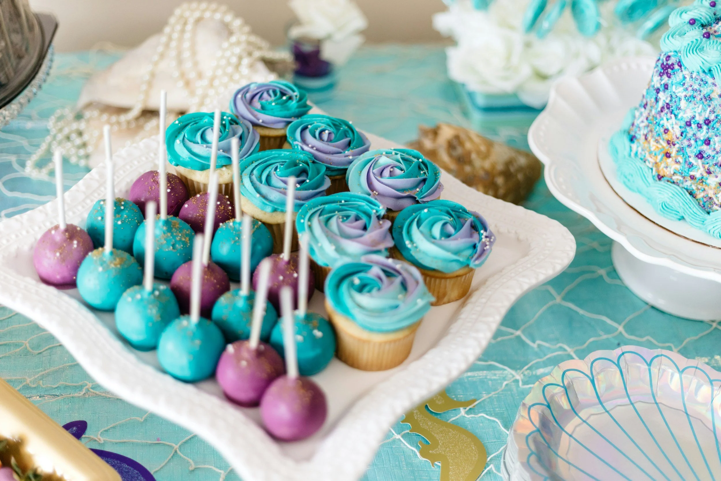 Luxury baby shower dessert table at Private Spa Luna, featuring custom, themed treats. Includes vibrant turquoise and purple cake pops and matching cupcakes with elegant blue and purple swirled frosting.