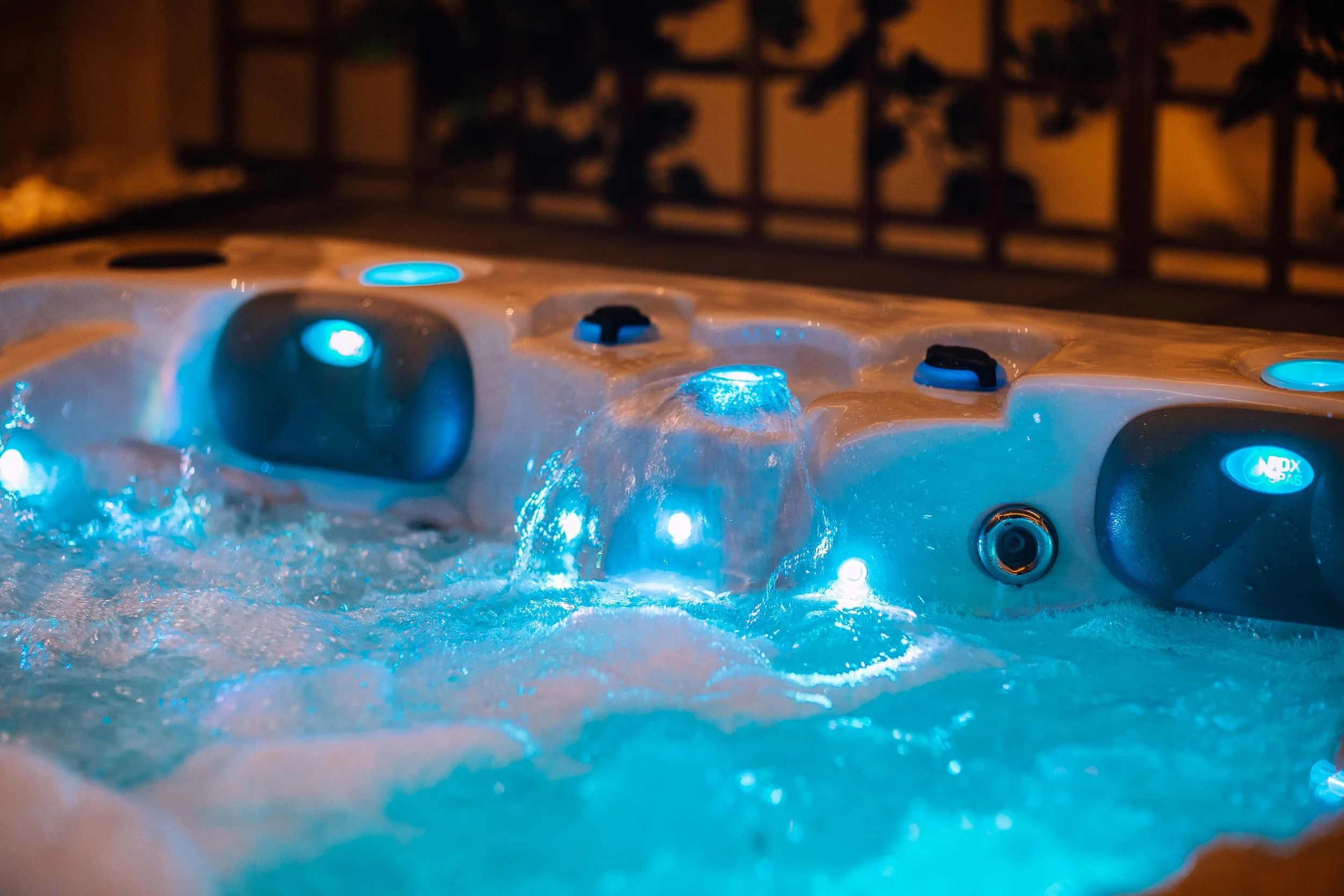A hot tub with blue LED lighting and bubbling water at night, surrounded by a wooden deck and fence.