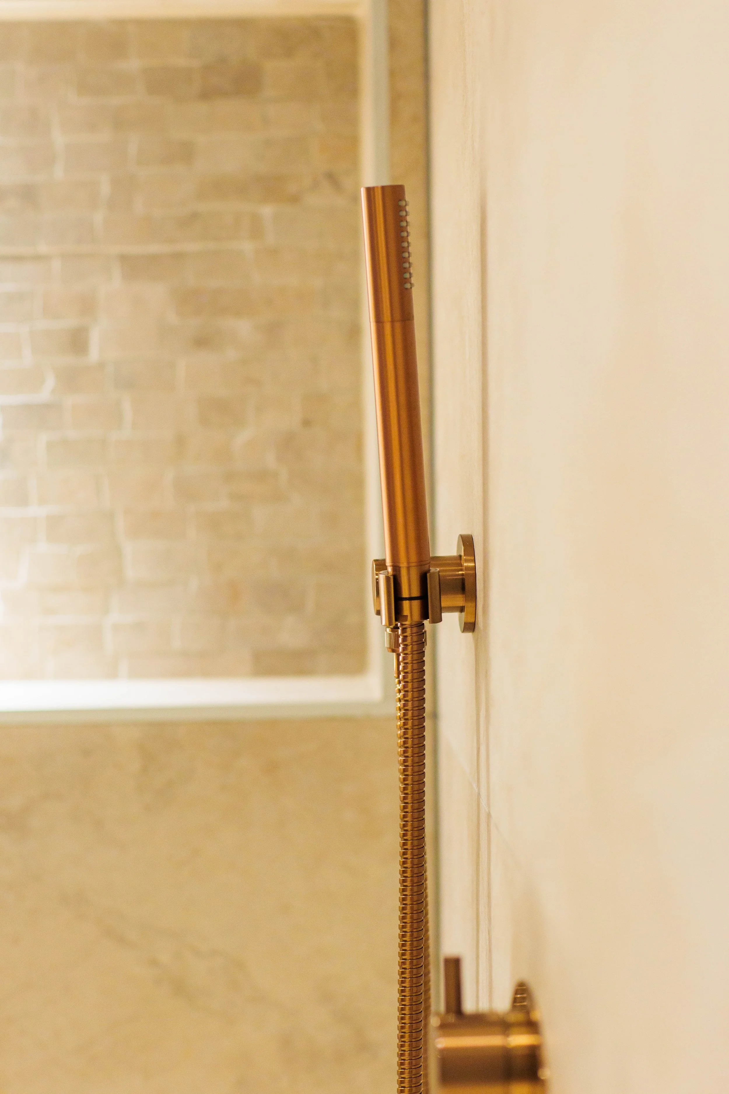 Close-up of a brushed gold showerhead mounted on a tiled wall.