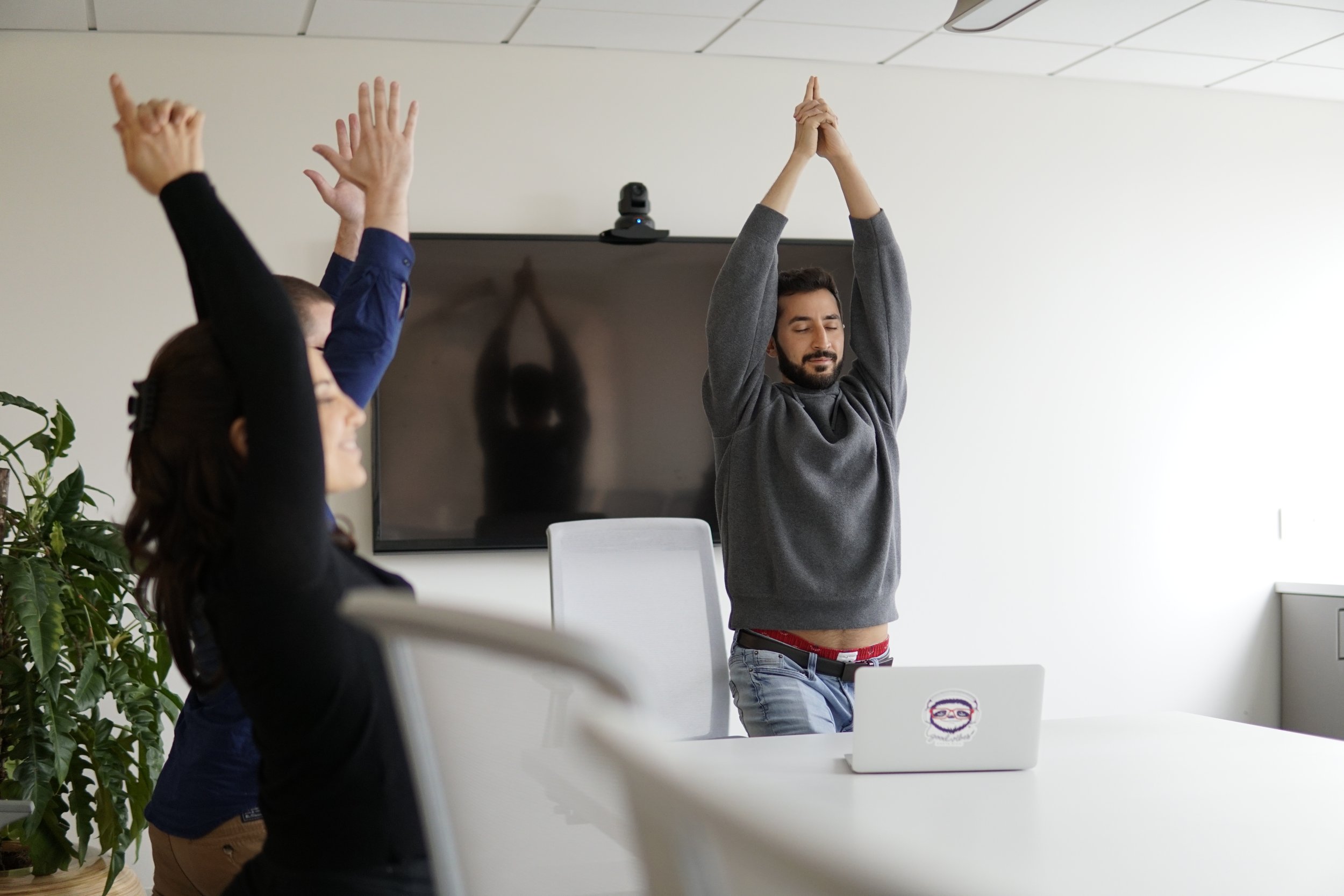 Group of employees in an meeting room for a hybrid yoga class.