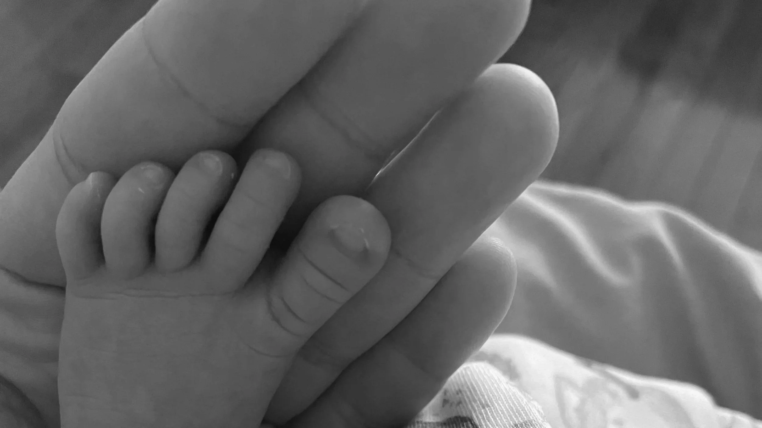 Close-up of a small child's hand gripping an adult's finger.