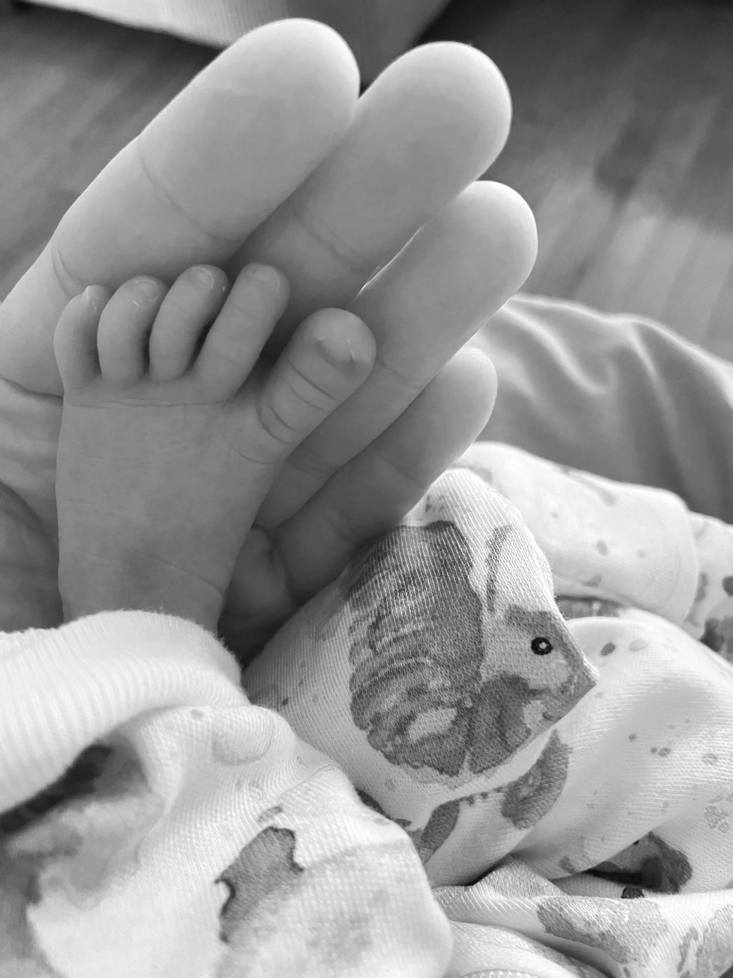 Close-up of a small child's hand holding an adult's finger, with the child's hand resting on a patterned fabric with a fish illustration.