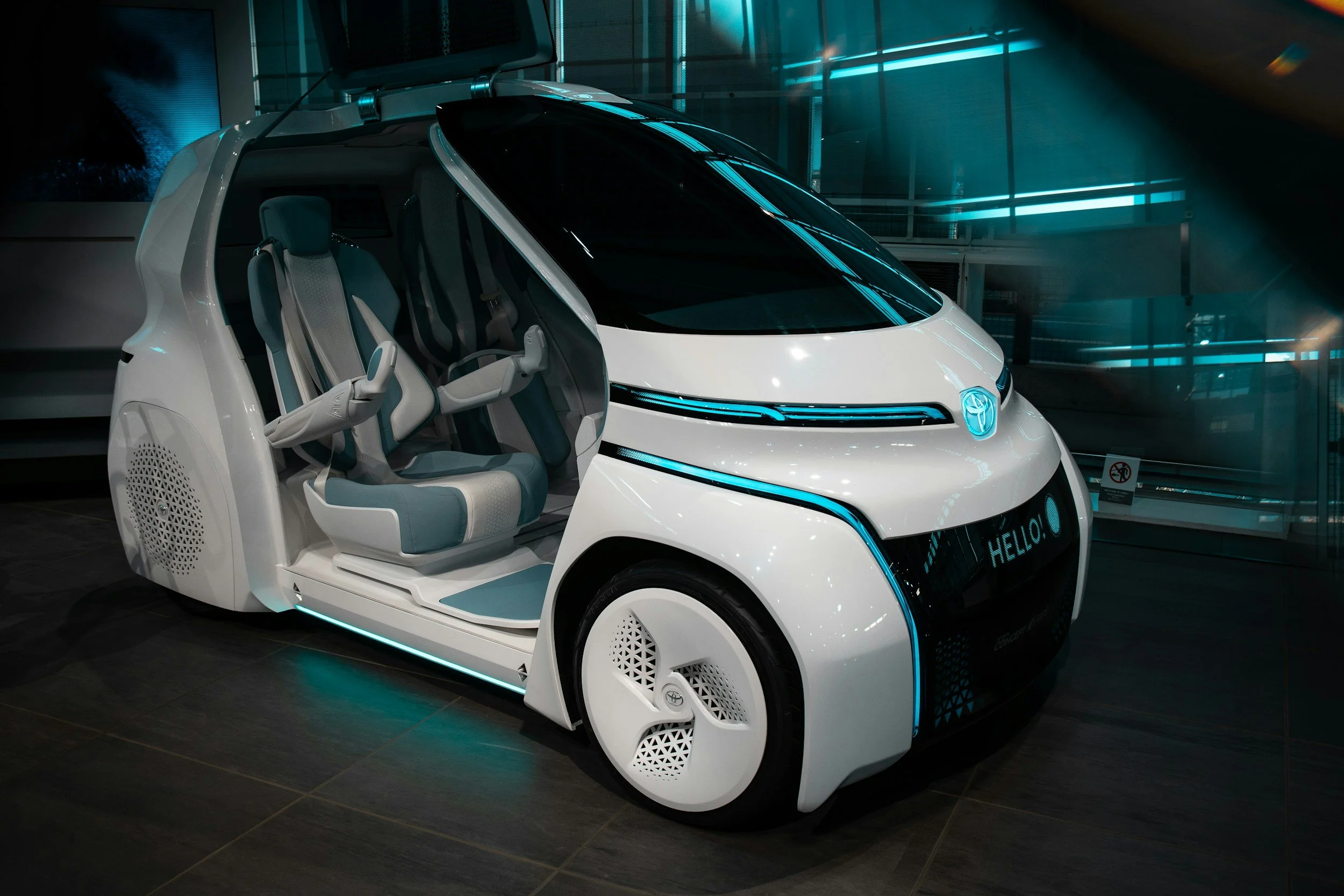 Futuristic white electric car with interior seats that look like airplane seats, displayed indoors with digital lighting accents.