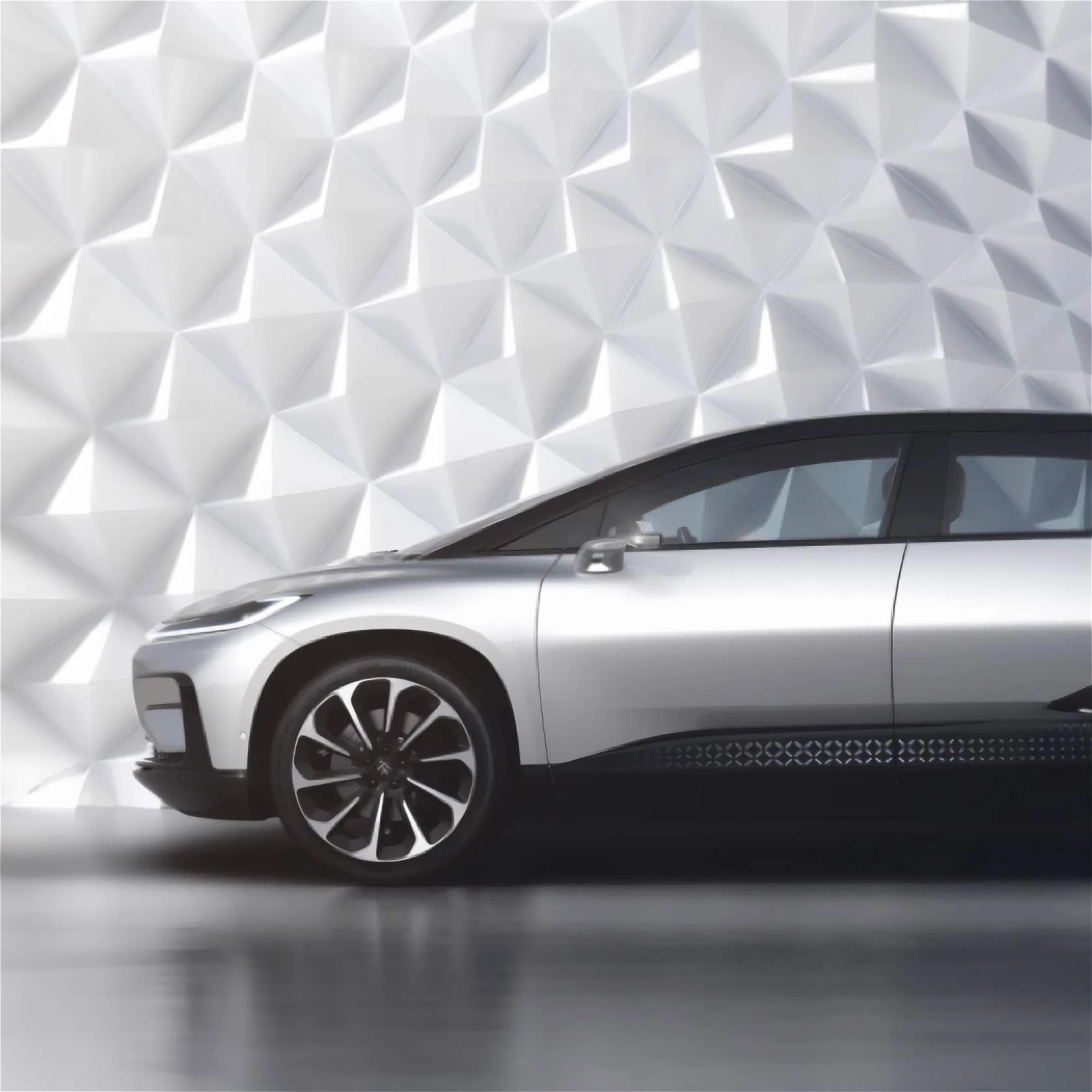 A silver electric car parked indoors against a white textured geometric wall.