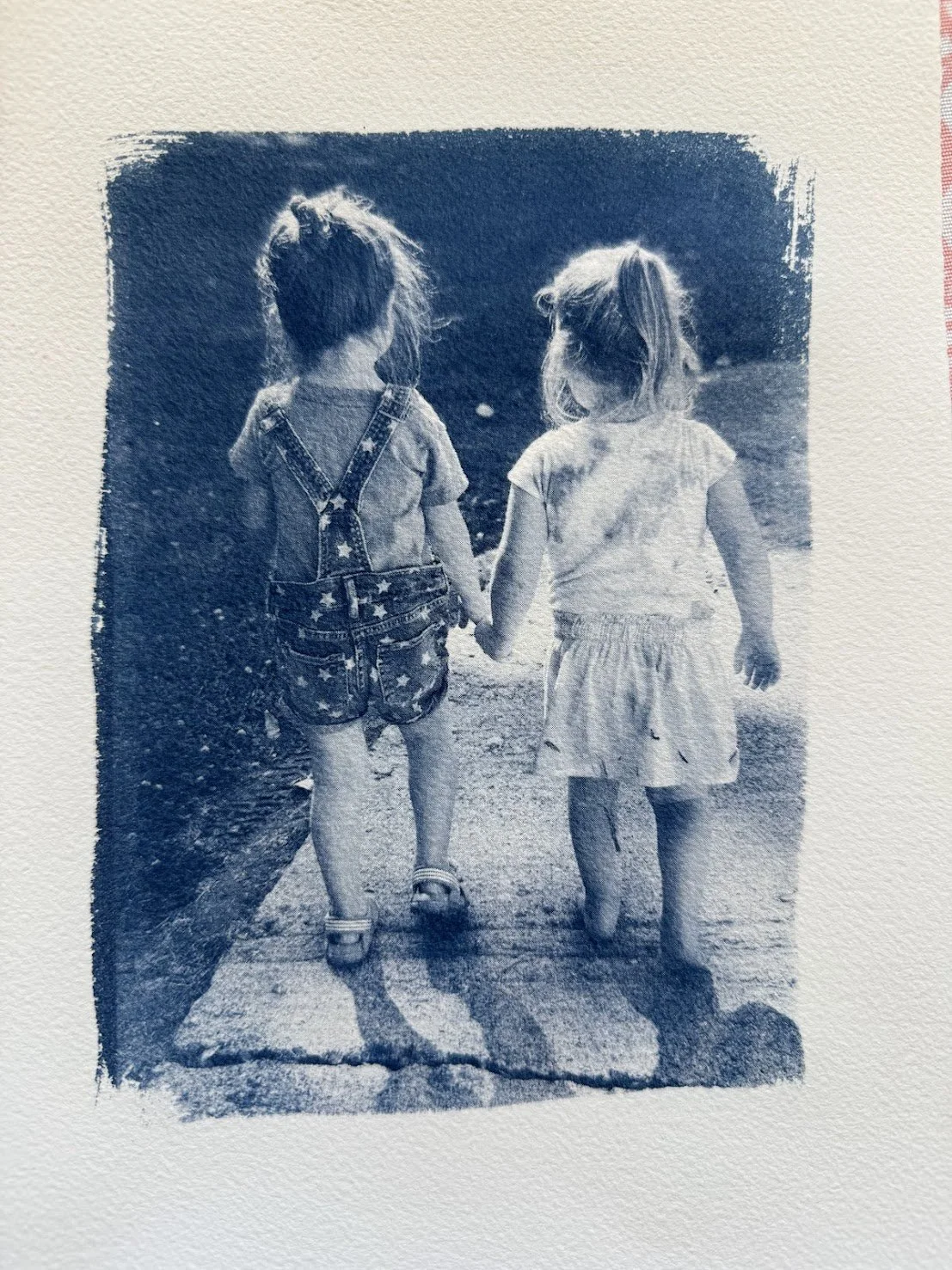 Two young girls walking hand in hand on a sidewalk, seen from behind.