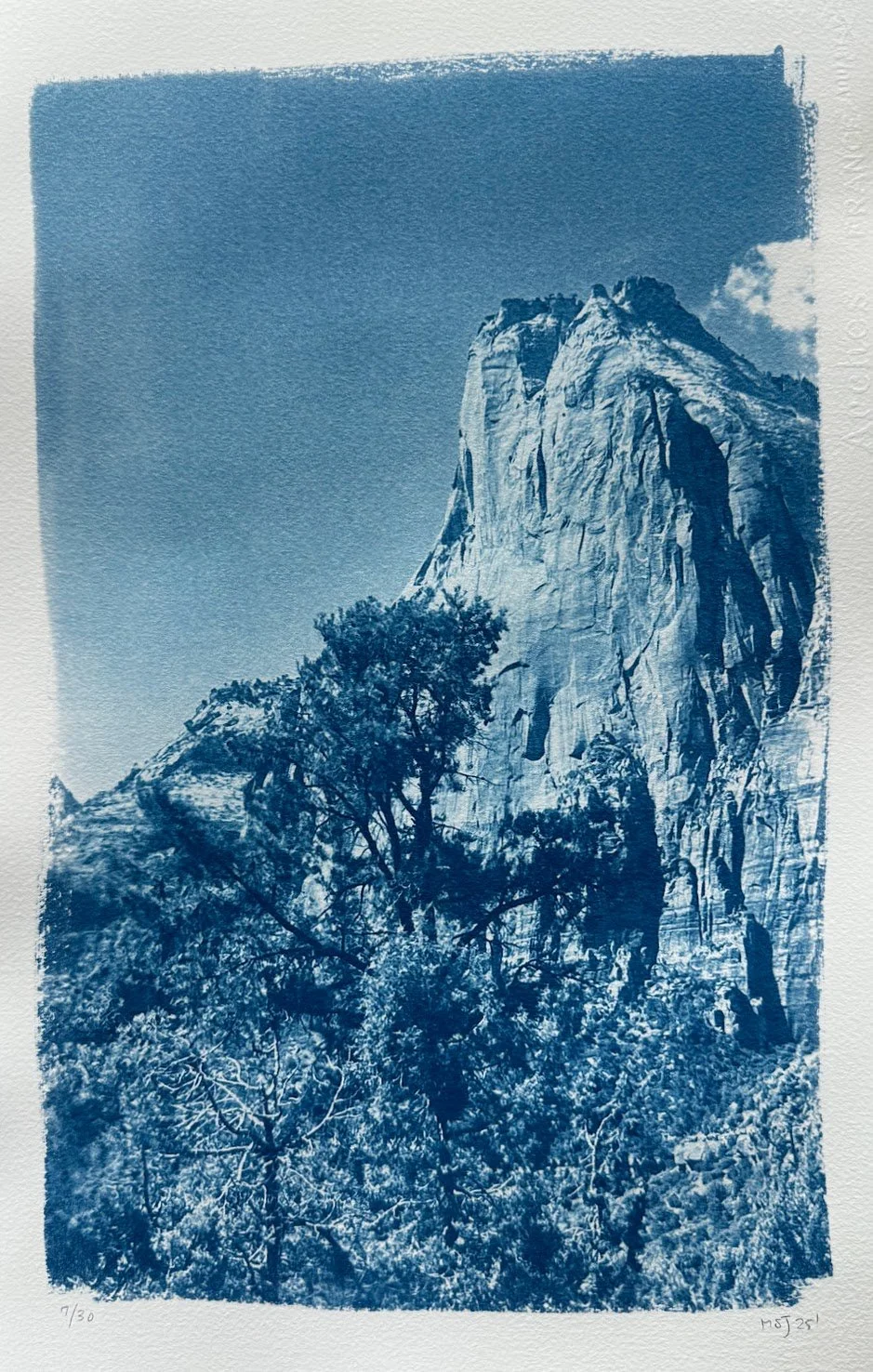 A monochromatic blue-toned print of a mountain peak with trees in the foreground.