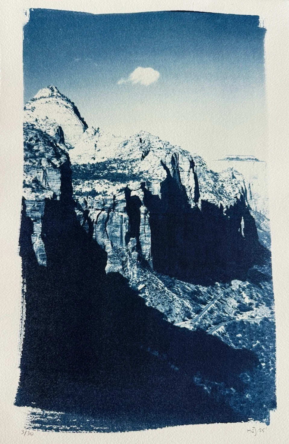 A monochrome blue-toned landscape featuring rugged, snow-capped mountains and tall, dark rocky cliffs with a small, solitary cloud in the sky.