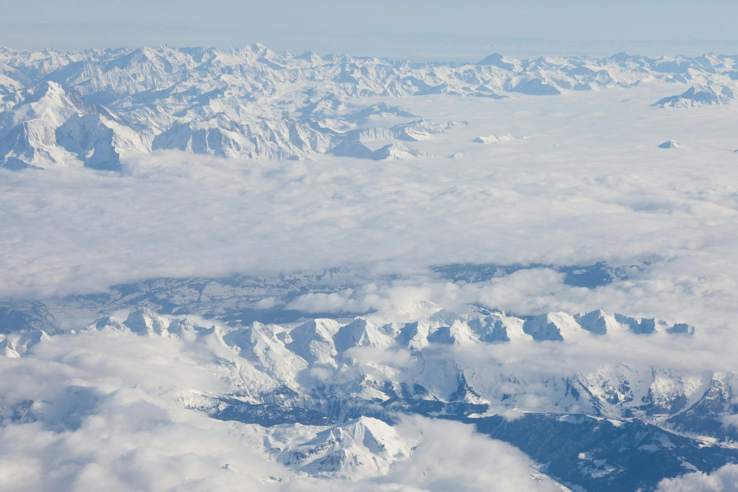 Aerial view of snow-covered mountains and glaciers with clouds in the sky.