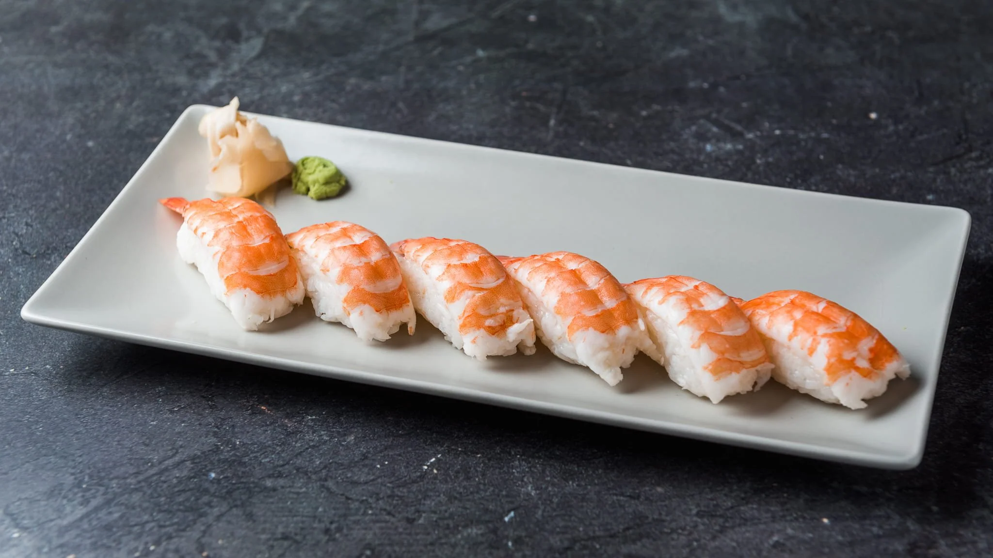 Sushi platter with seven pieces of shrimp nigiri, served with wasabi and pickled ginger on a white rectangular plate.