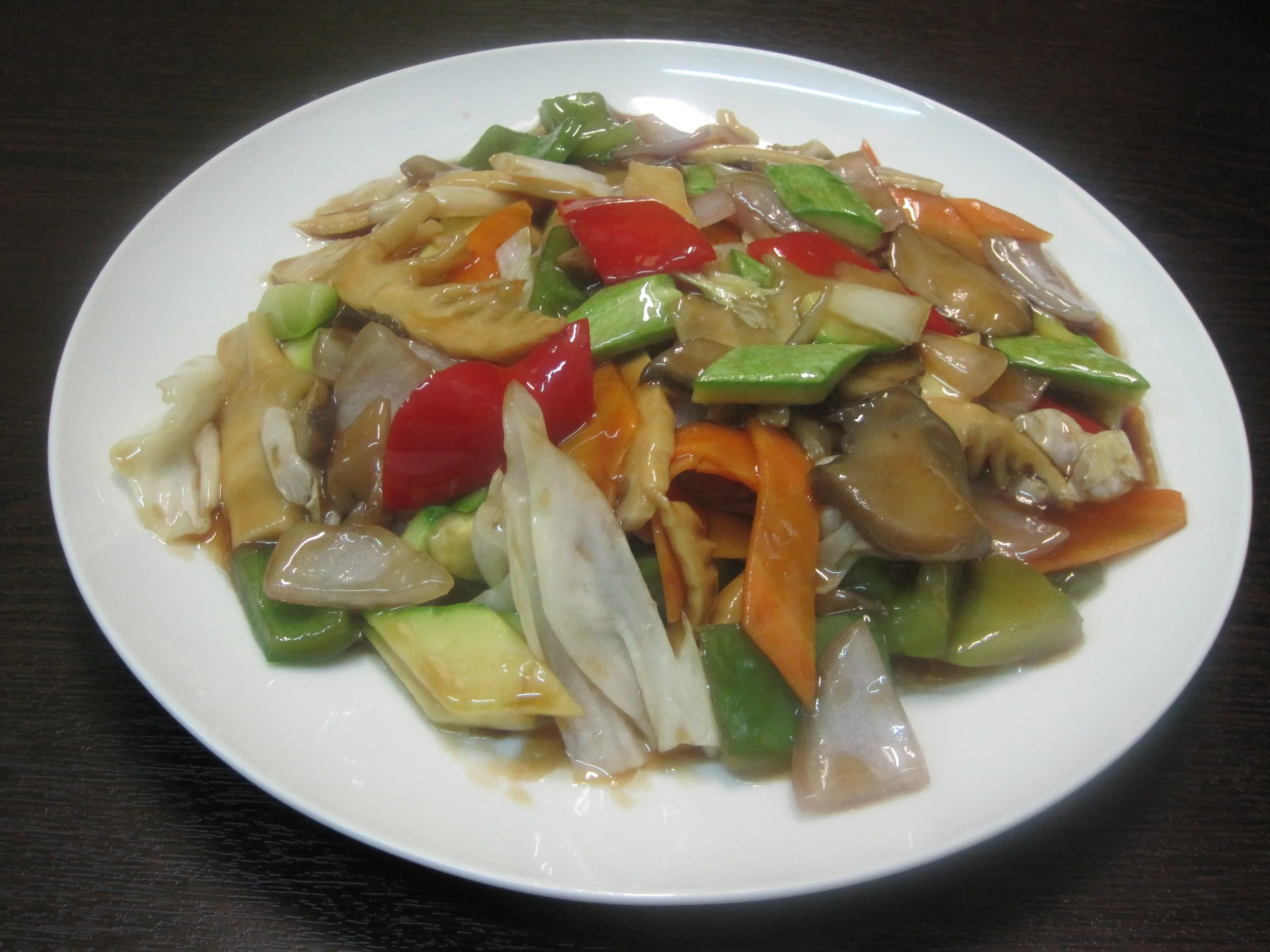 A white plate filled with stir-fried mixed vegetables including red and green bell peppers, carrots, onions, and mushrooms, on a dark wooden surface.