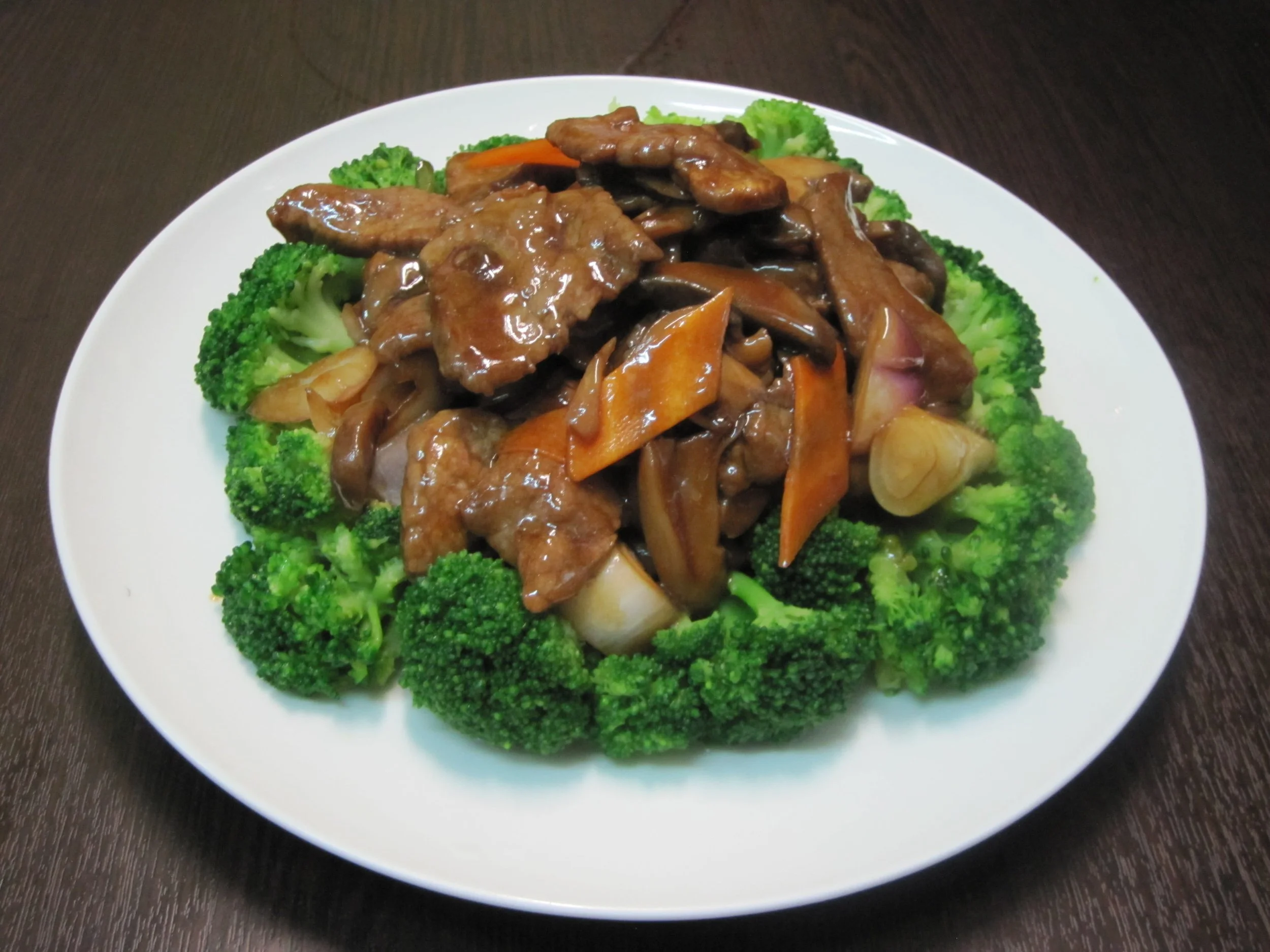 Plate of stir-fried beef and vegetables with broccoli, carrots, onions, and mushrooms in a sauce on a white dish.