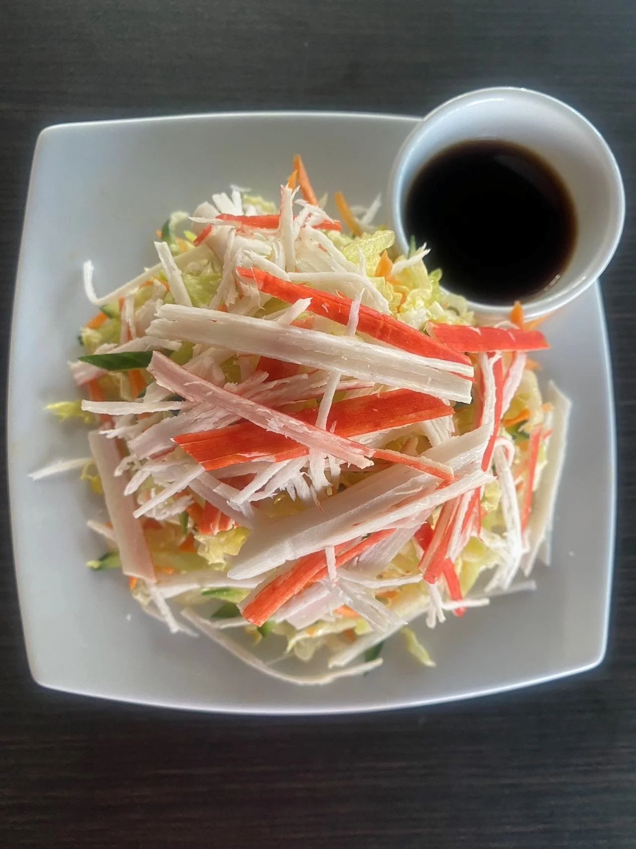 A plate of shredded crab salad with a cup of soy sauce.