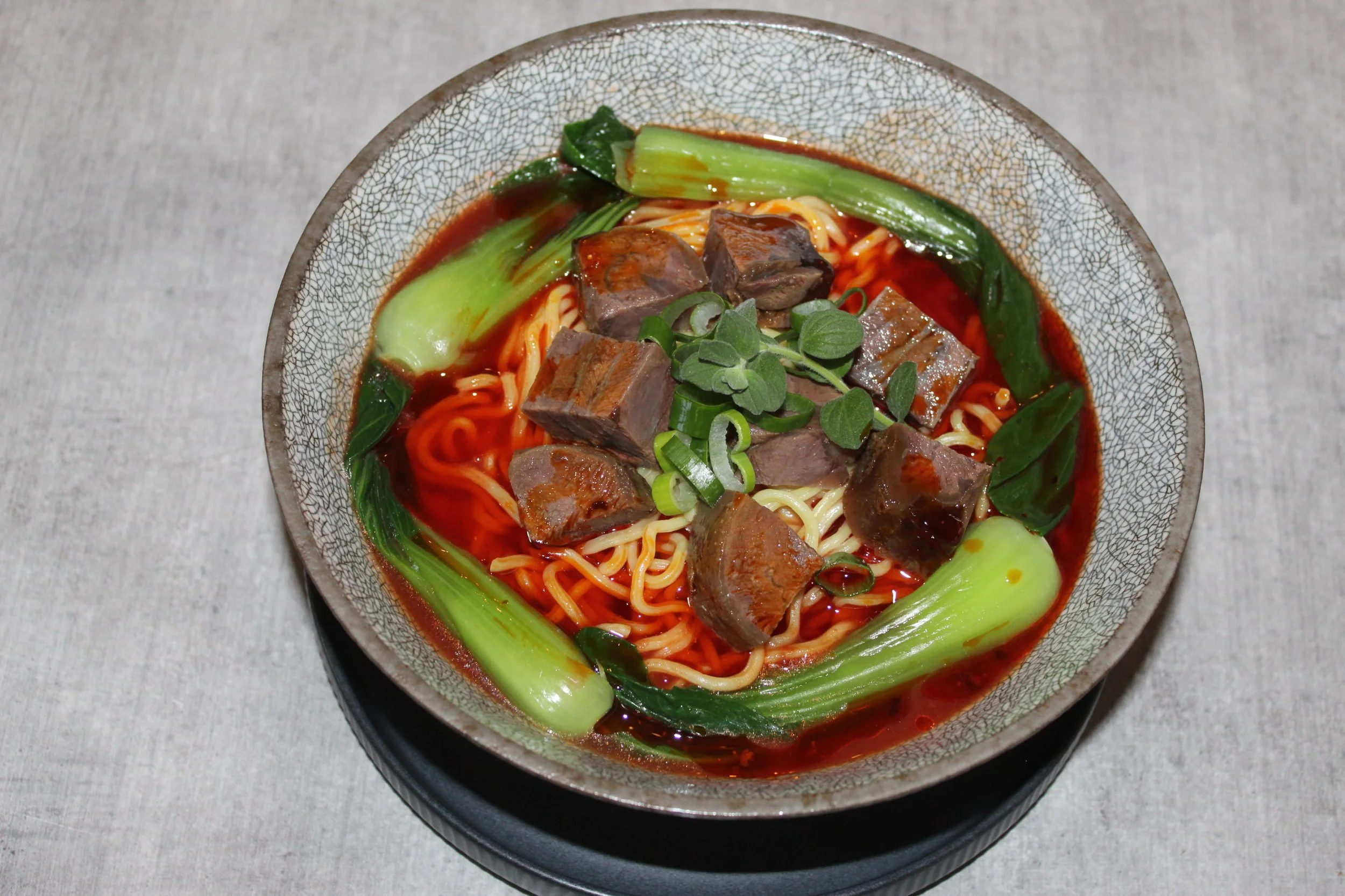 Bowl of ramen noodles with beef chunks, green onions, and bok choy in a red broth.