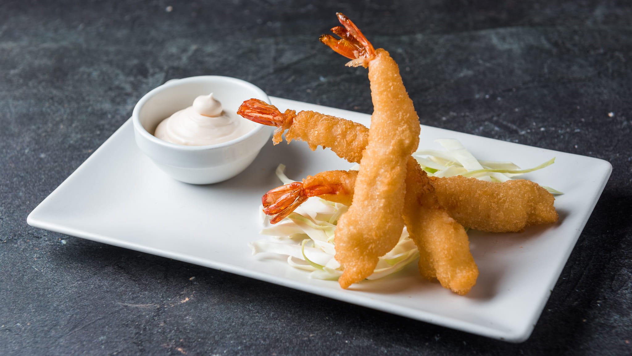 Plate with three fried shrimp on shredded lettuce, and a small bowl of creamy dipping sauce on the side