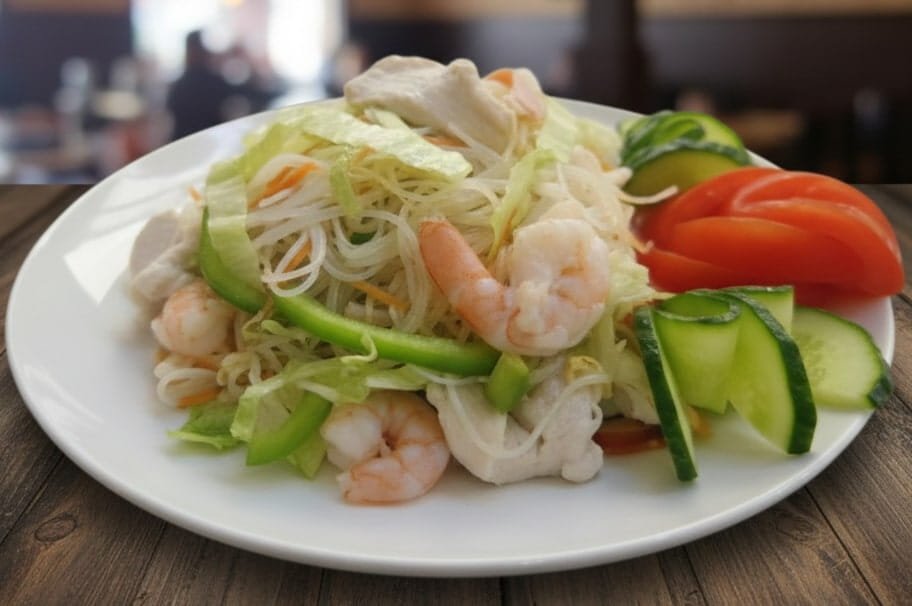Plate of shrimp salad with shredded vegetables, cucumbers, tomatoes, and lettuce.