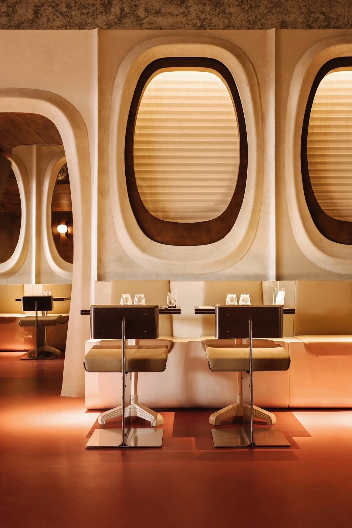 Salle à manger dans un restaurant avec des tables, des chaises et des verres en verre sur la table, mur avec fenêtres ovales et décoration moderne.