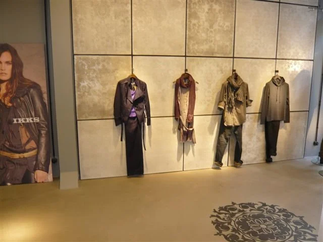 Vêtements suspendus sur un mur dans une boutique de mode, à gauche une affiche publicitaire avec une femme
