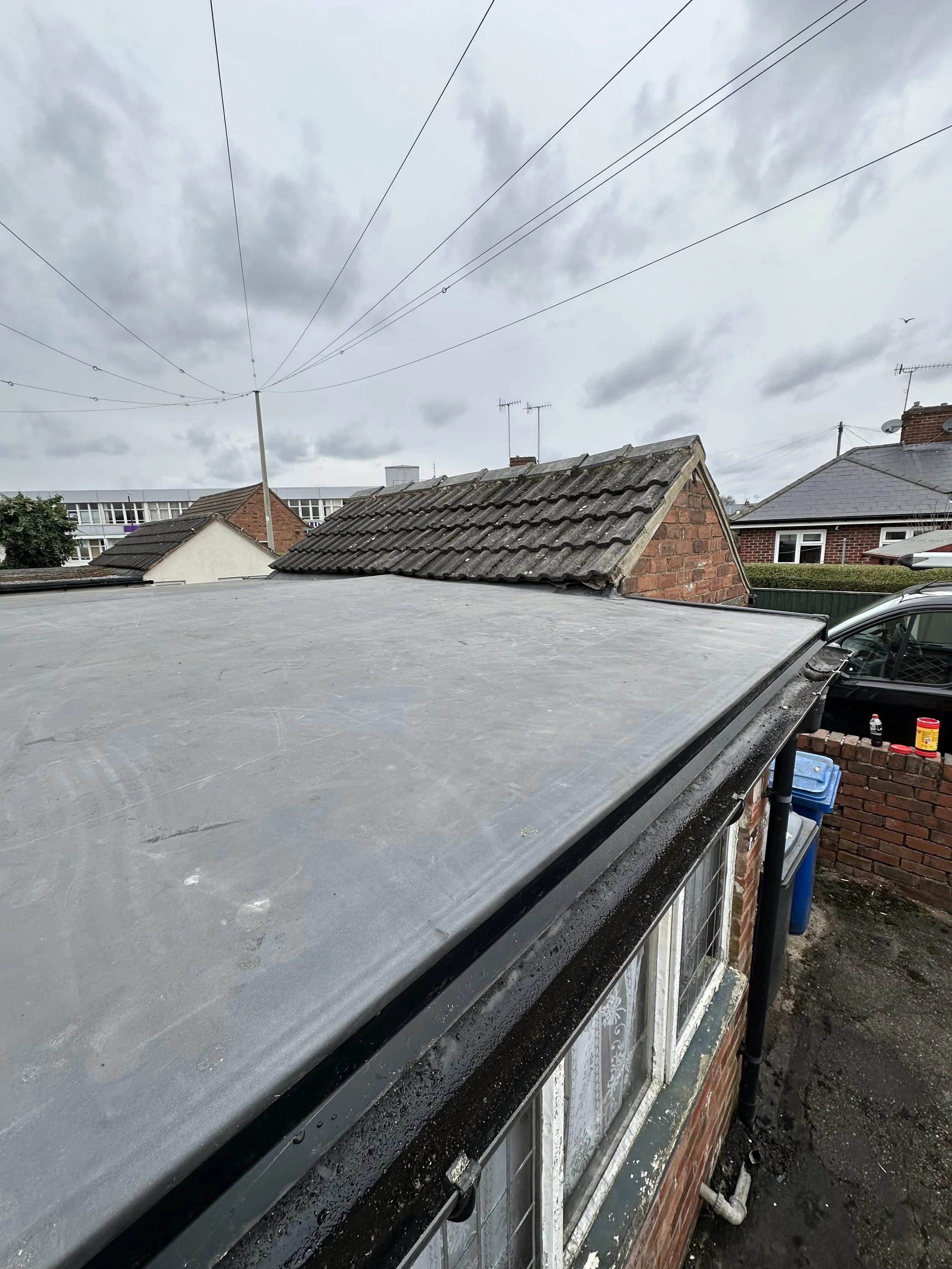 View from a rooftop showing cloudy sky, neighboring houses with brick and tiled roofs, and power lines overhead.